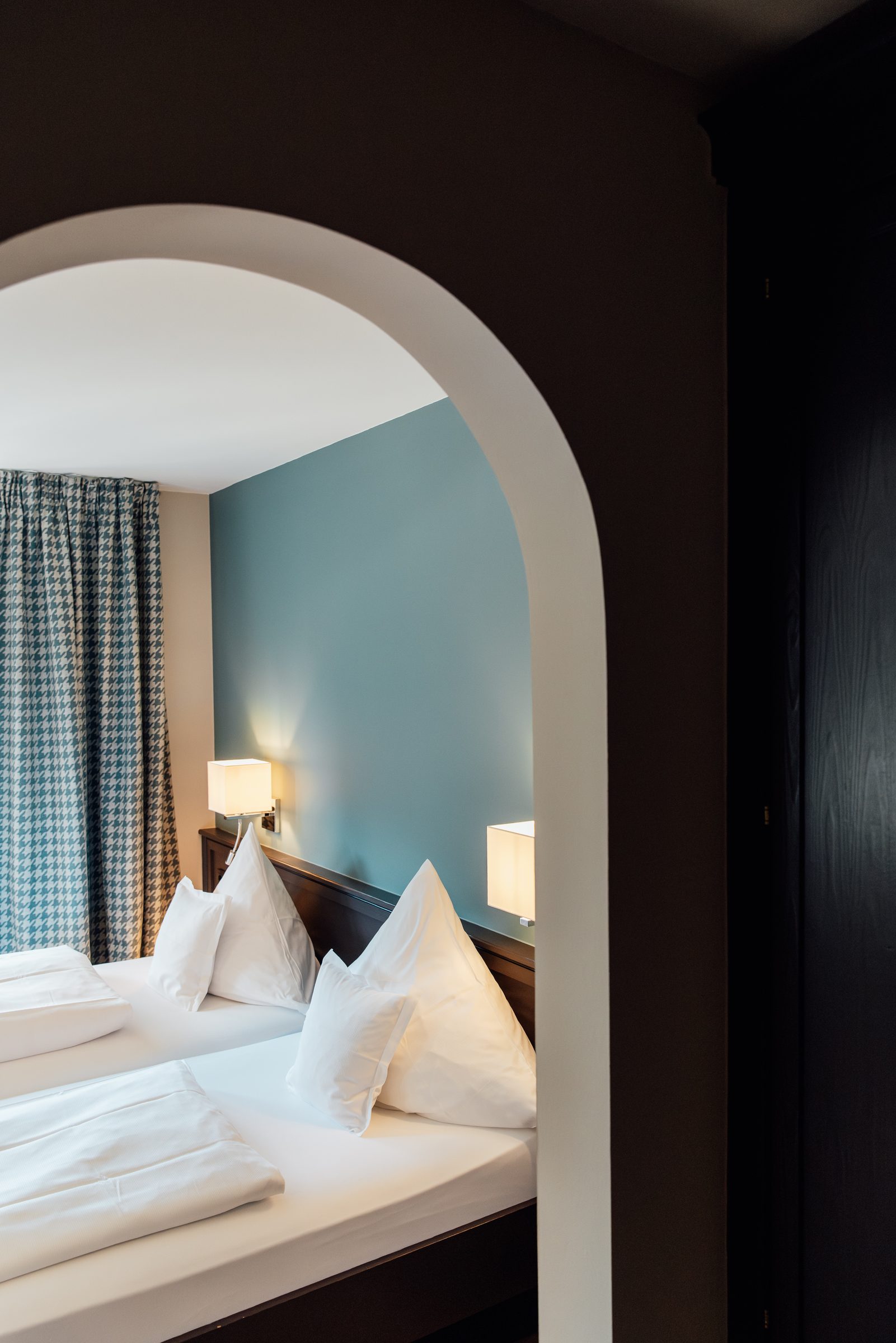 Blick durch einen Rundbogen in ein helles Hotelzimmer im Hotel Krone mit Doppelbett und hellblauer Wand
