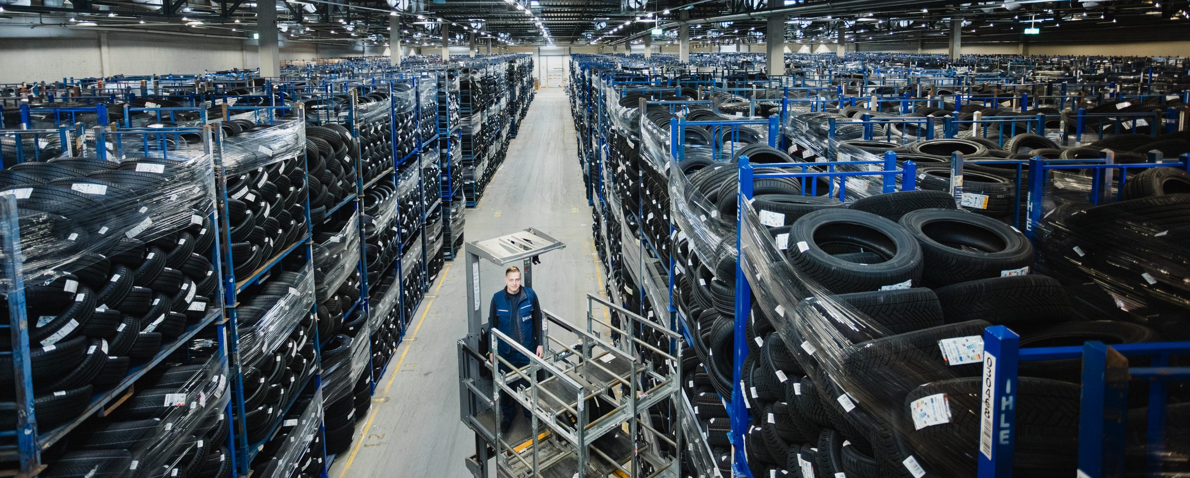 Weiter Blick über die Reifenregale im Lager von IHLE, in der Mitte ein Mitarbeiter auf einem Kommissioniergerät