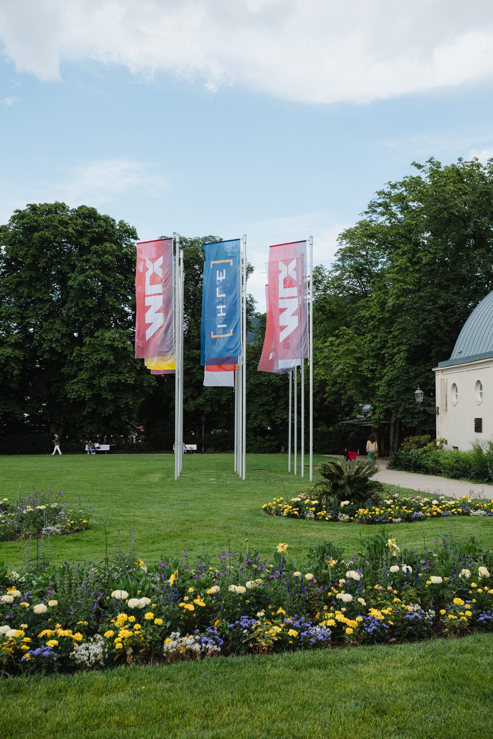 Fahnen mit dem Logo der Tagung vor einem Park mit Blumenbeet