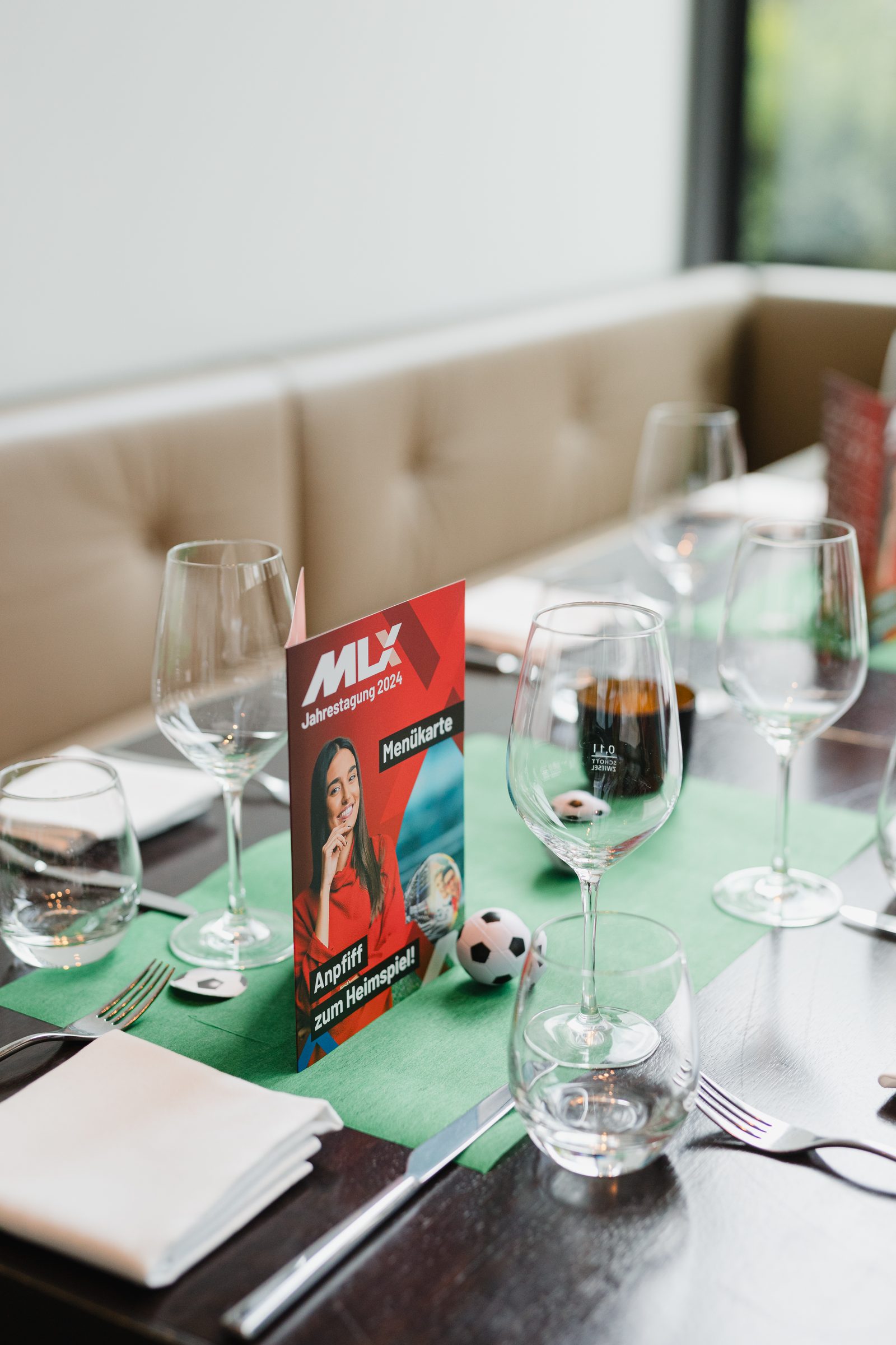 Gedeckter Tisch der Tagung mit Weingläsern, kleinen Fußbällen und einer Menükarte mit dem Titel Anpfiff zum Heimspiel