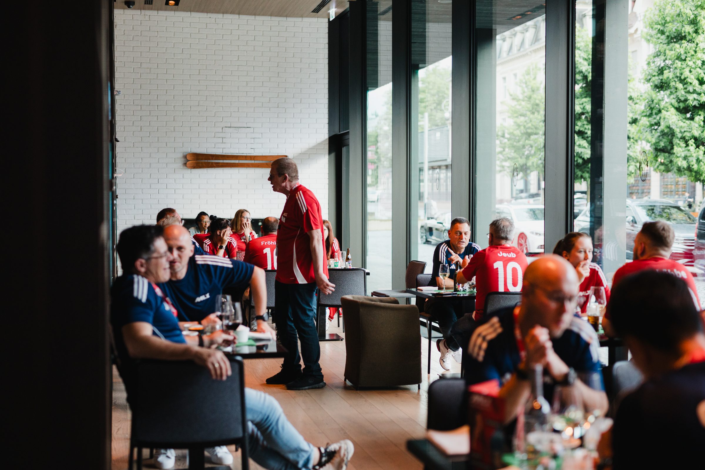 Gäste der Tagung in roten und blauen Trikots sitzen in einer Lounge mit großen Fenstern und unterhalten sich
