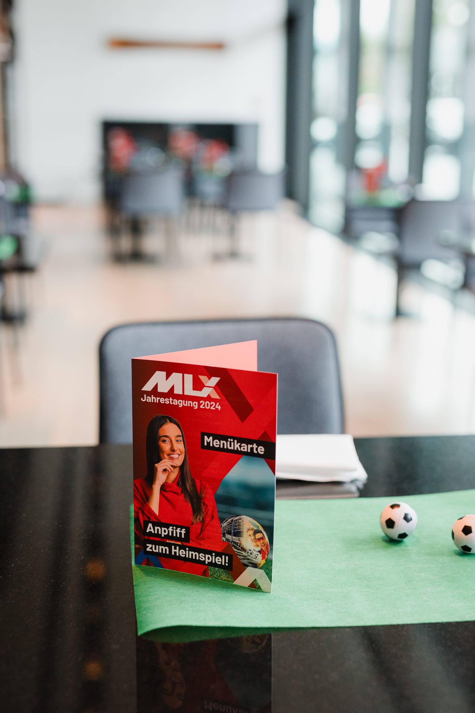 Menükarte der Tagung mit dem Titel Anpfiff zum Heimspiel auf einem Tisch mit grünem Läufer und kleinen Fußbällen