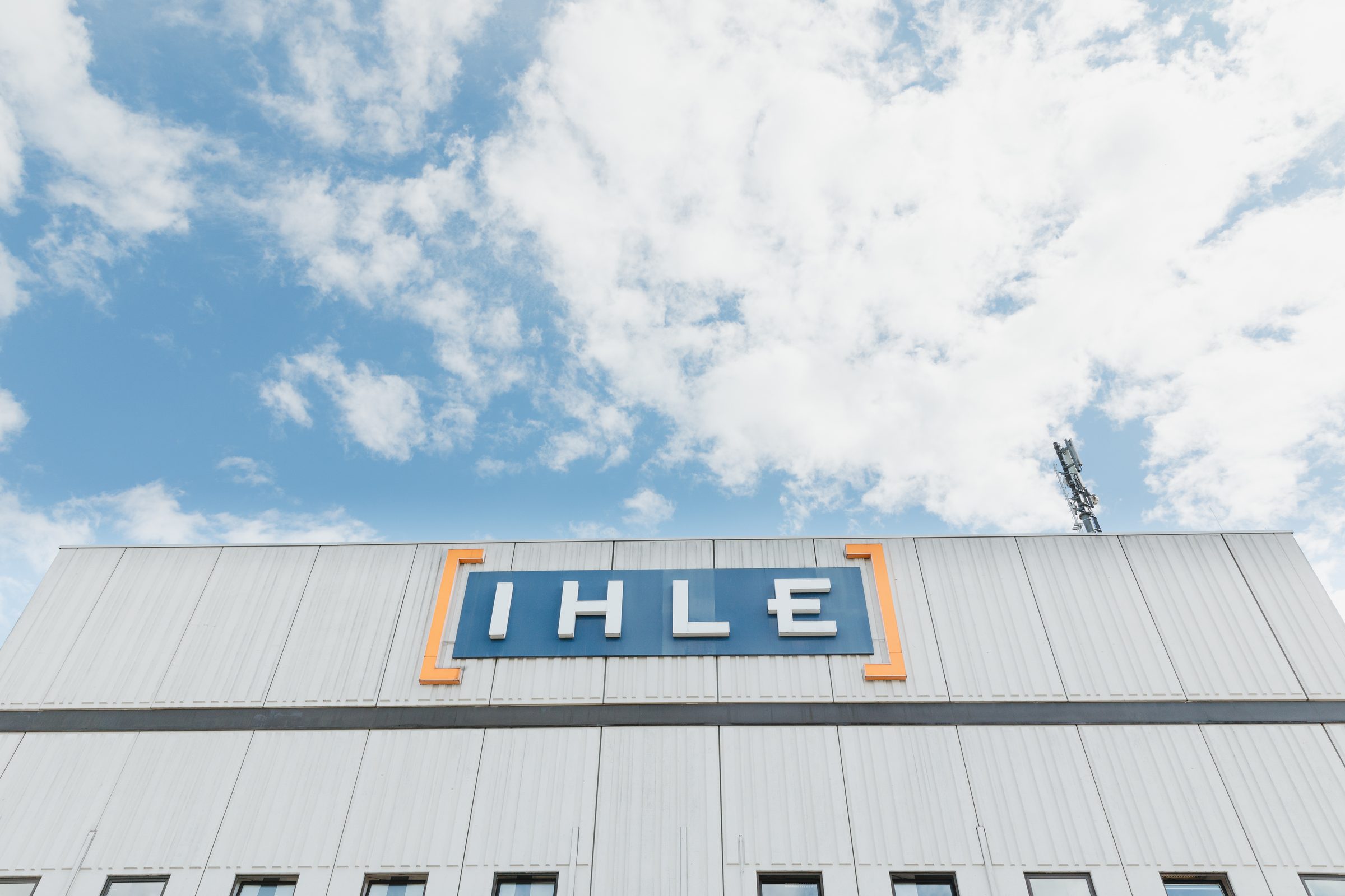 Schriftzug von IHLE auf dem Dach einer Halle vor blauem Himmel mit Wolken