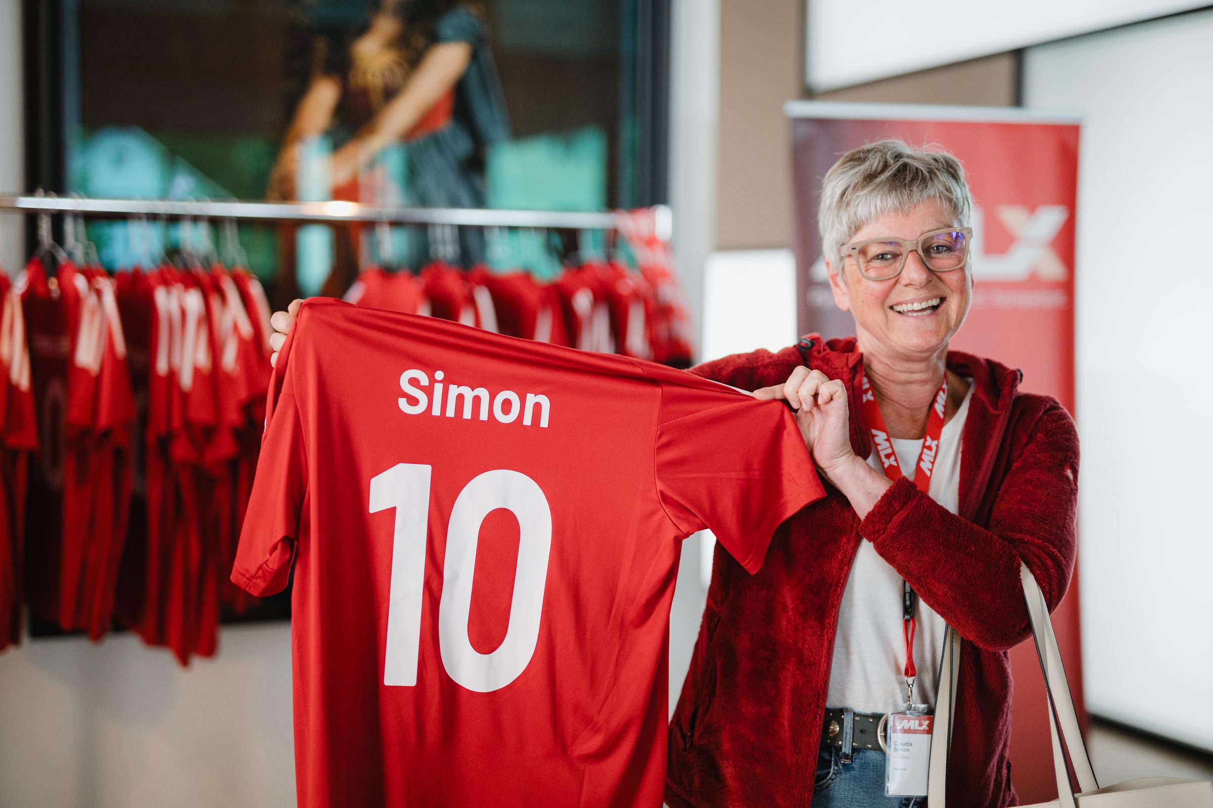 Teilnehmerin der Tagung hält lachend ein rotes Fußballtrikot mit Namen und Rückennummer hoch