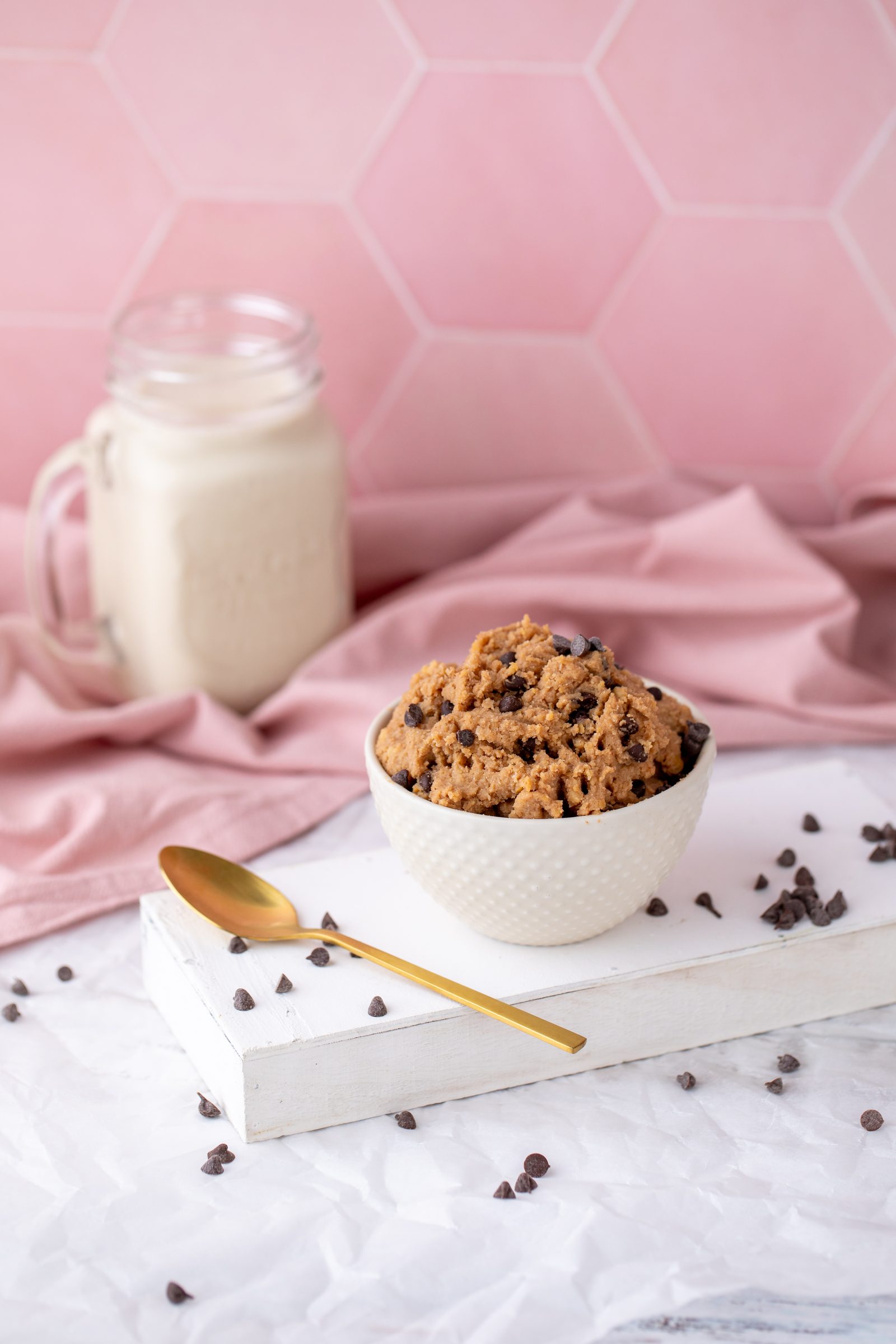 Cookie Dough mit Schokotropfen in einer weißen Schale vor rosa Fliesen, daneben ein goldener Löffel und ein Glas Milch, Rezeptfoto für ein GU-Kochbuch