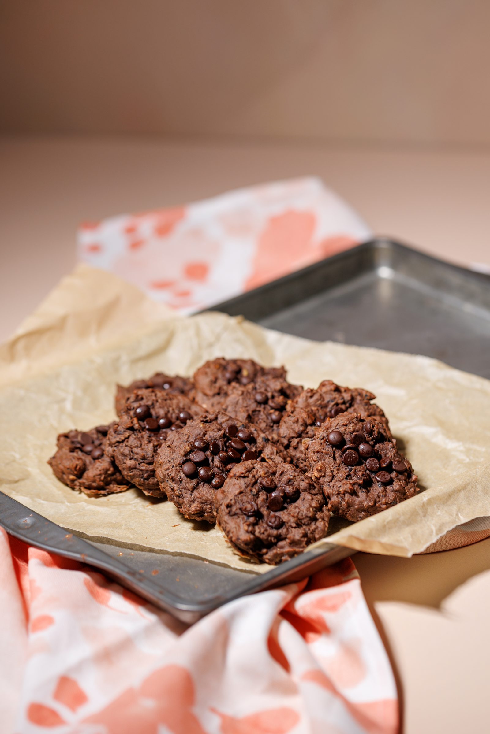 Chocolate Chip Cookies auf Backpapier und einem Backblech, darunter ein rosa gemustertes Tuch, Rezeptfoto für ein GU-Kochbuch