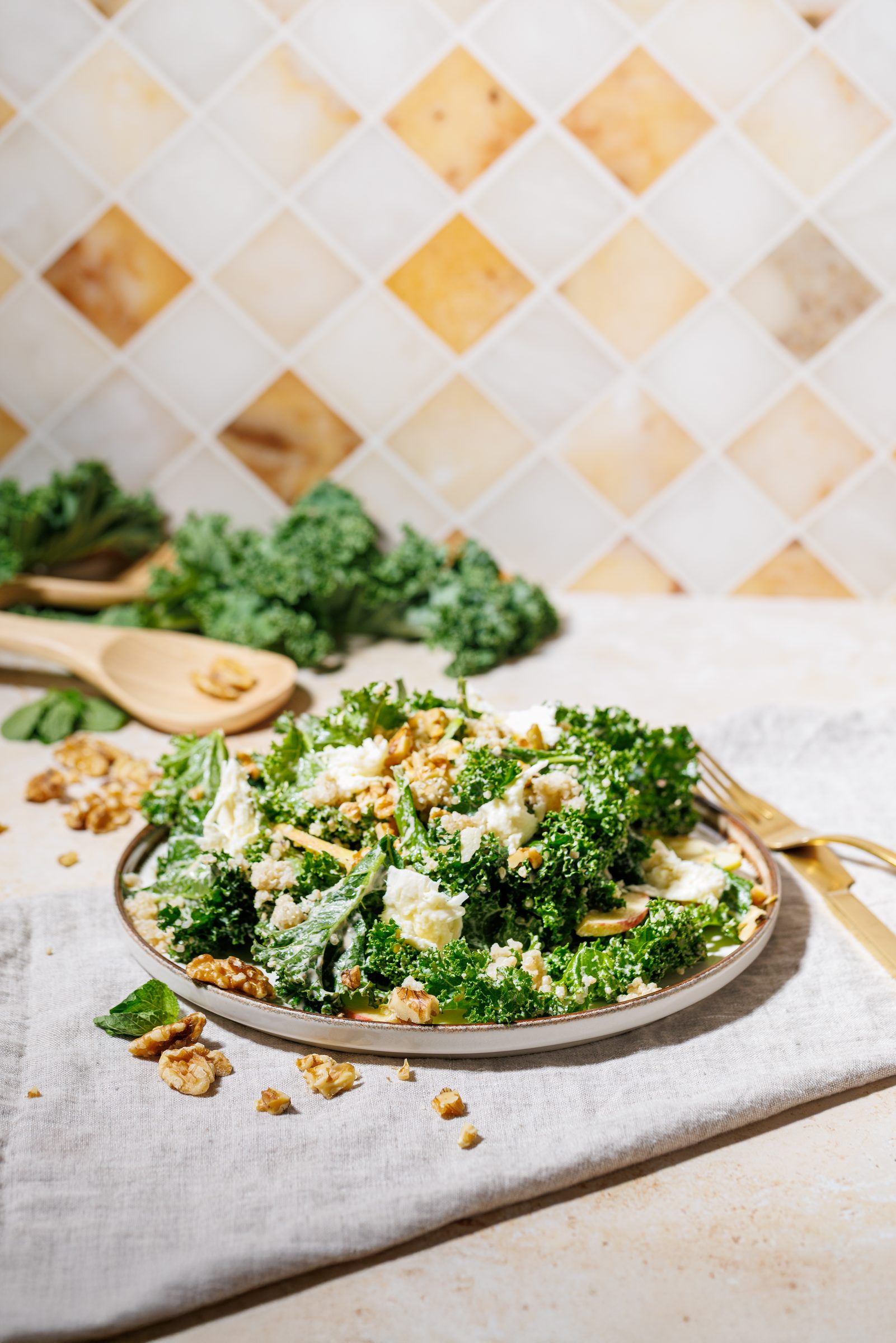 Quinoa-Grünkohl-Salat mit Walnüssen auf einem Teller vor gelb gemusterten Fliesen, Rezeptfoto für ein GU-Kochbuch
