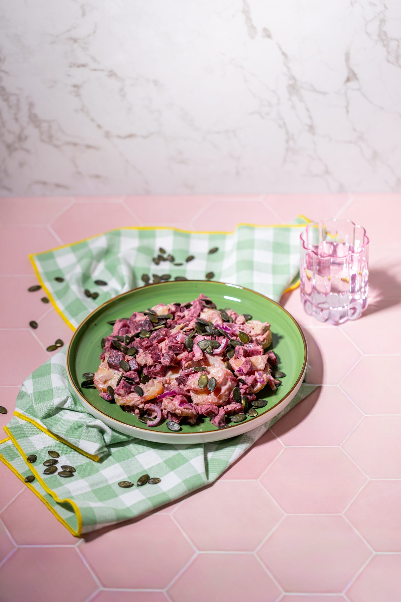Roter Kartoffelsalat mit Thunfisch und Kürbiskernen auf einem grünen Teller vor rosa Fliesen, Rezeptfoto für ein GU-Kochbuch