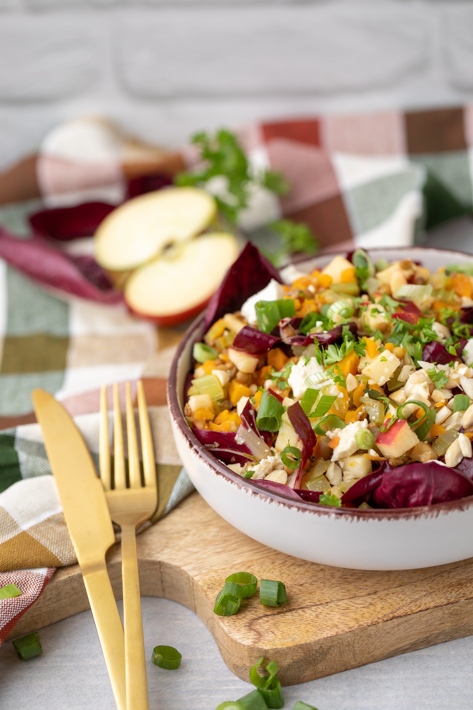 Linsen-Apfel-Salat mit Radicchio in einer Schale auf einem Holzbrett, daneben goldenes Besteck und ein halbierter Apfel, Rezeptfoto für ein GU-Kochbuch