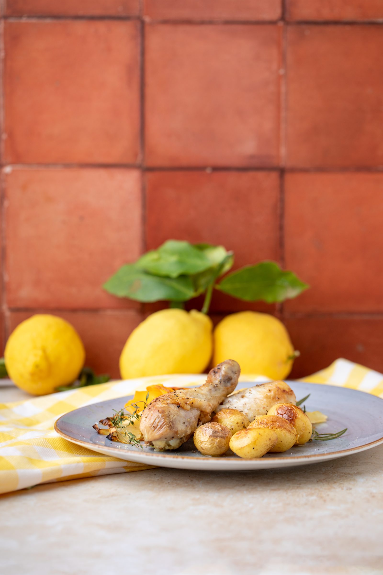 Zitronenhühnchen mit Kartoffeln auf einem Teller vor Terrakottafliesen und Zitronen, Rezeptfoto für ein GU-Kochbuch
