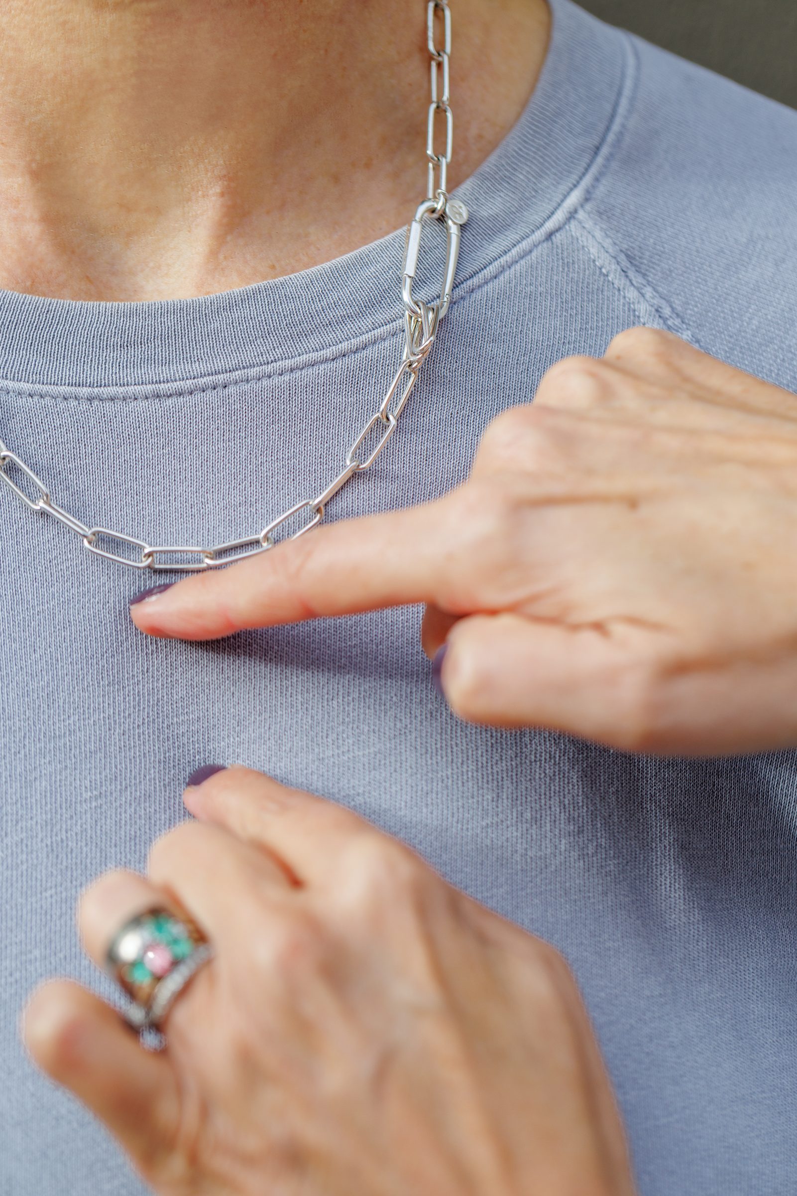 Finger zeigt auf eine silberne Gliederkette von Lilienglück mit großem Verschluss auf einem blauen Pullover