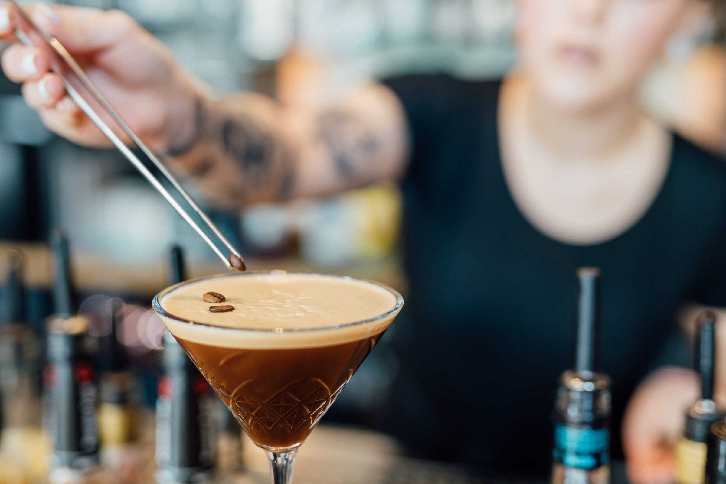 Barkeeperin garniert mit einer Pinzette einen Cocktail an der Bar