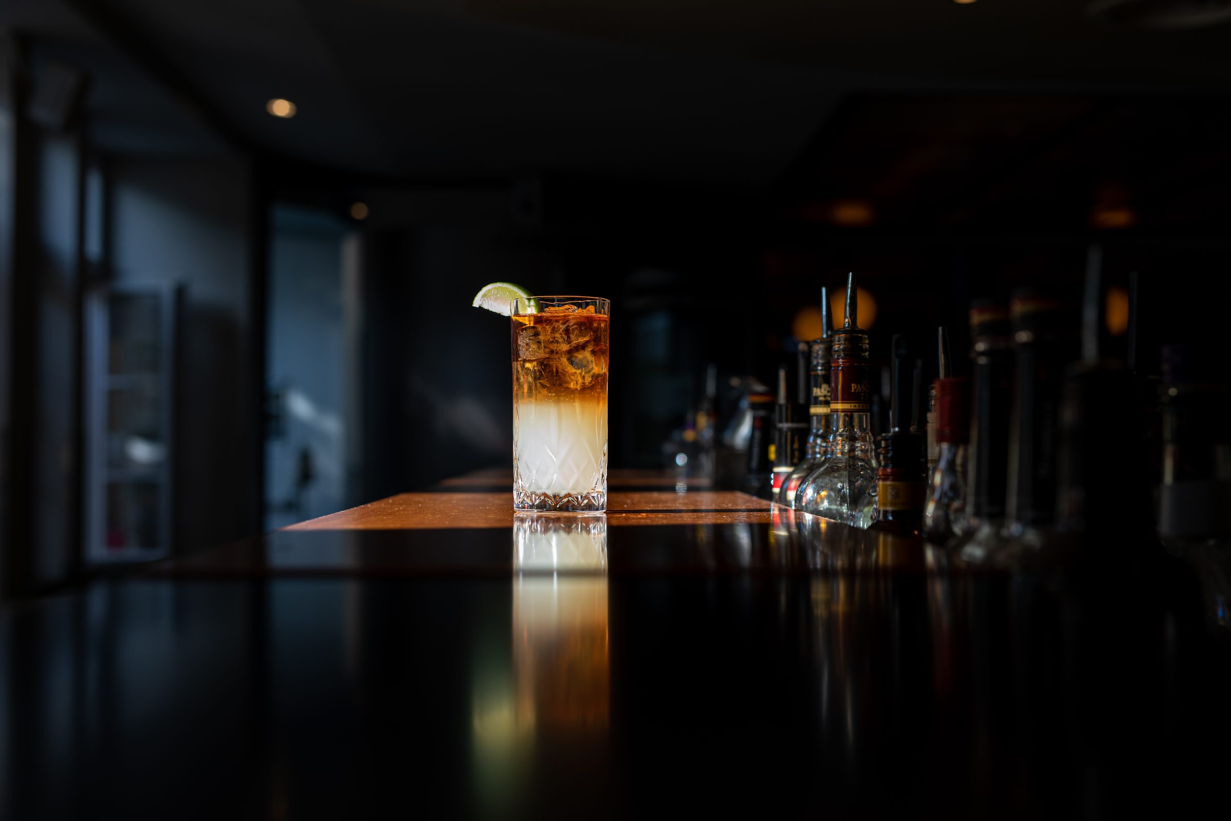 Longdrink mit Limette auf dem spiegelnden Tresen der abendlich dunklen Bar des Ludwig in Mosbach, dahinter Flaschen