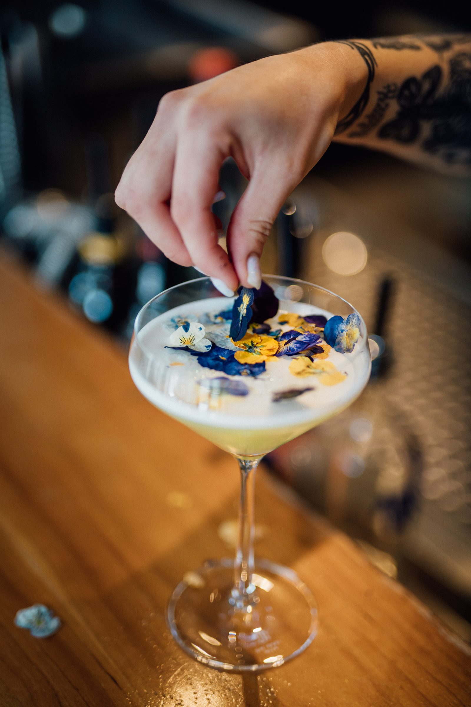 Hand legt essbare Blüten auf einen hellen Cocktail mit Schaumkrone auf dem Bartresen des Ludwig in Mosbach