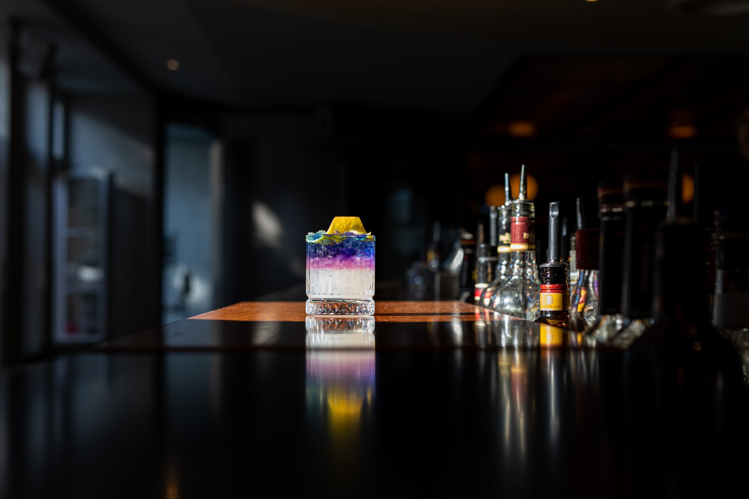 Violett geschichteter Cocktail im Tumbler auf dem spiegelnden Tresen der dunklen Bar des Ludwig in Mosbach