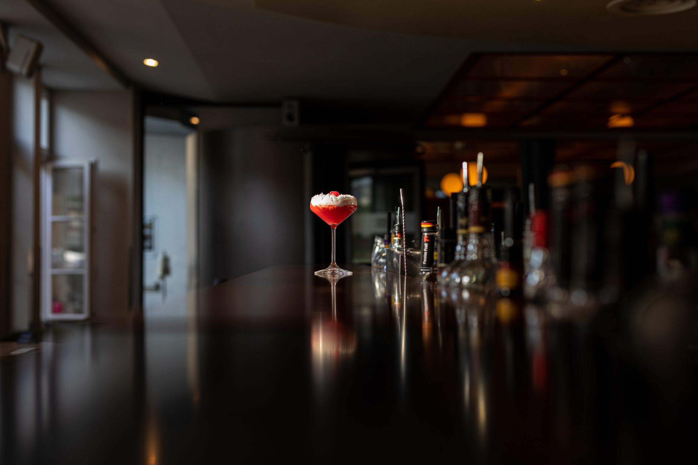 Roter Cocktail mit Schaumkrone und Himbeere in einer Cocktailschale auf dem spiegelnden Tresen der dunklen Bar des Ludwig in Mosbach