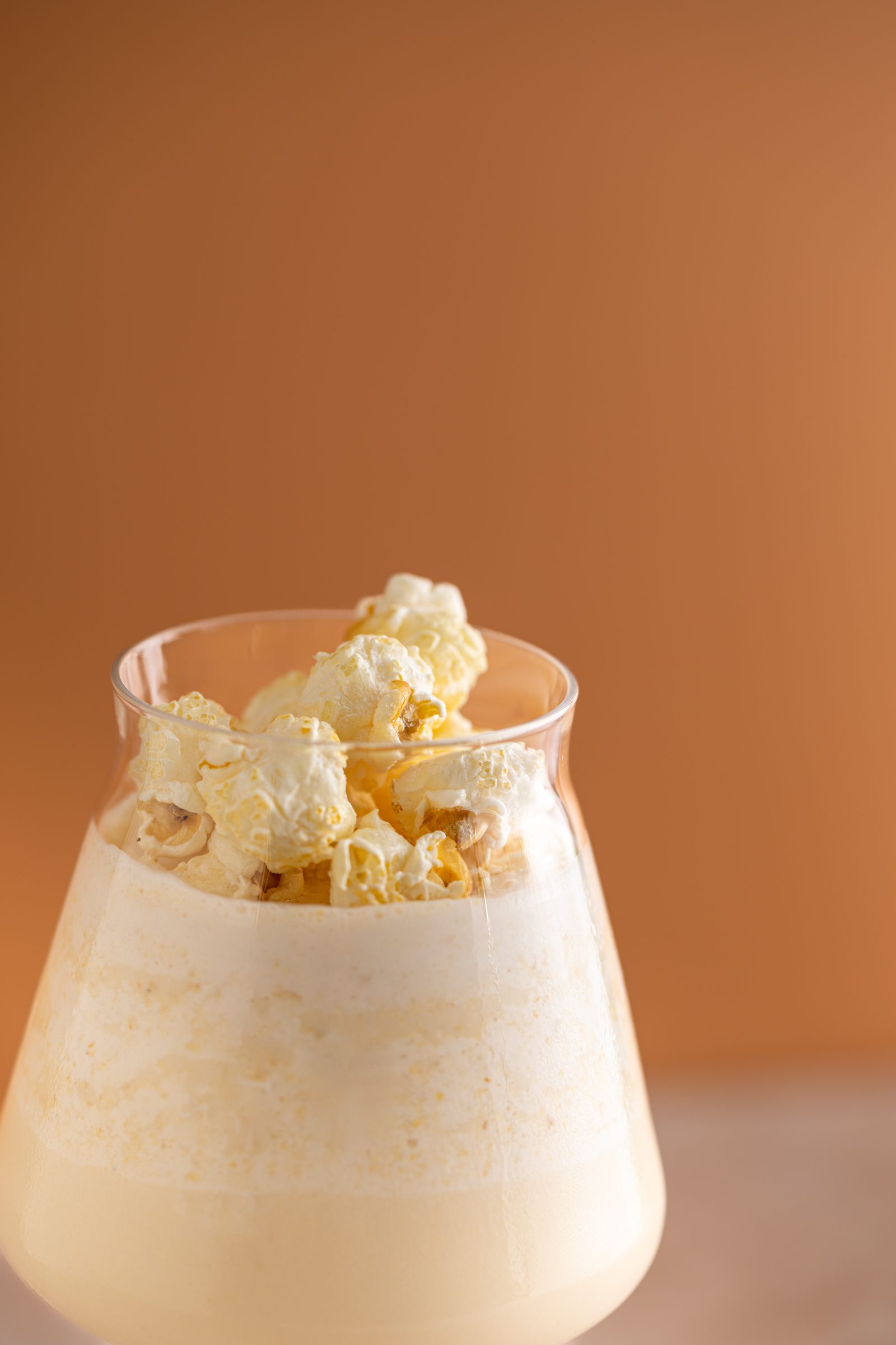 Cremiger Cocktail mit Popcorn im bauchigen Glas vor orangefarbenem Hintergrund, Cocktailfoto für das Ludwig in Mosbach