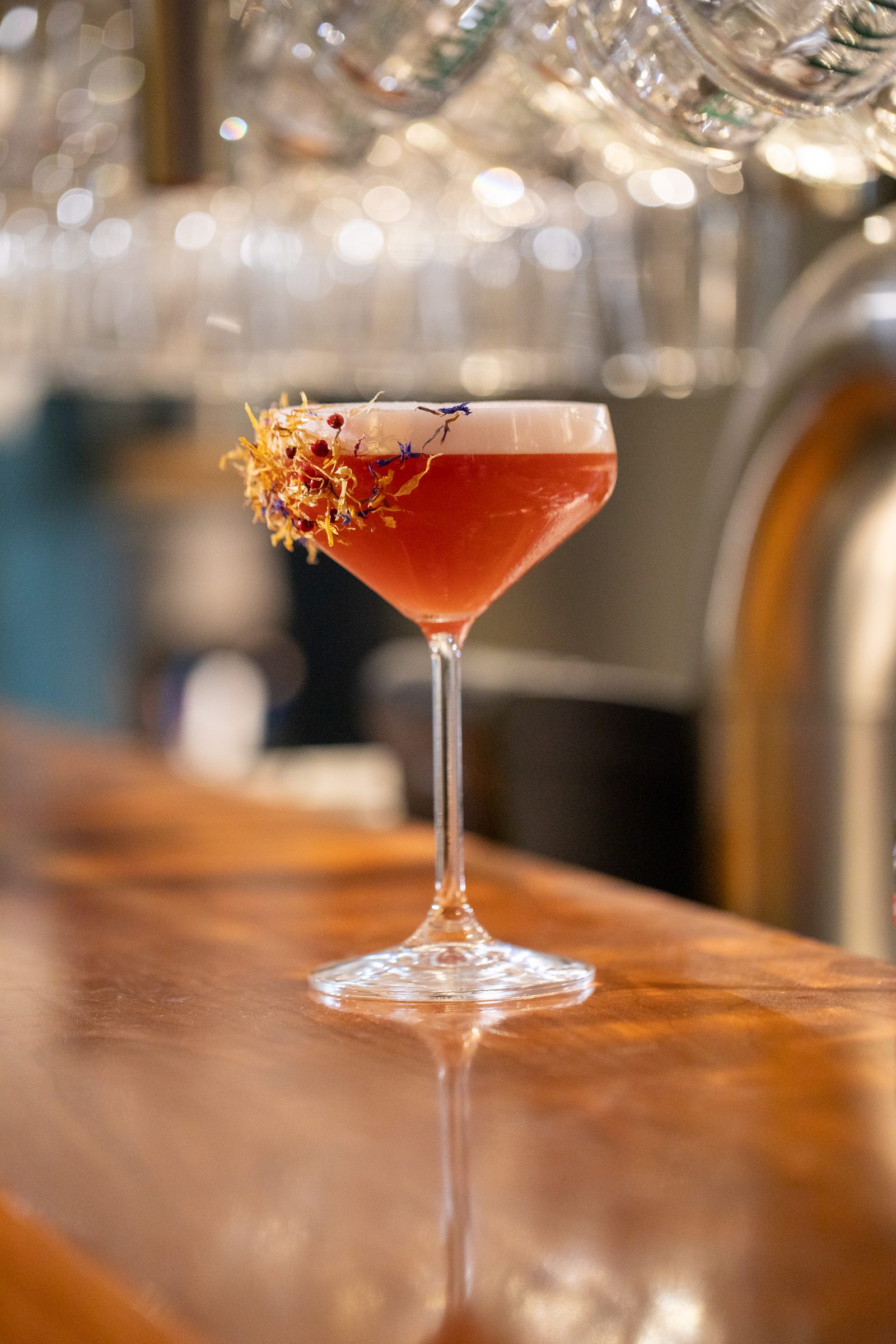 Roter Cocktail mit Blütengarnitur in einer Cocktailschale auf dem Holztresen der Bar des Ludwig in Mosbach