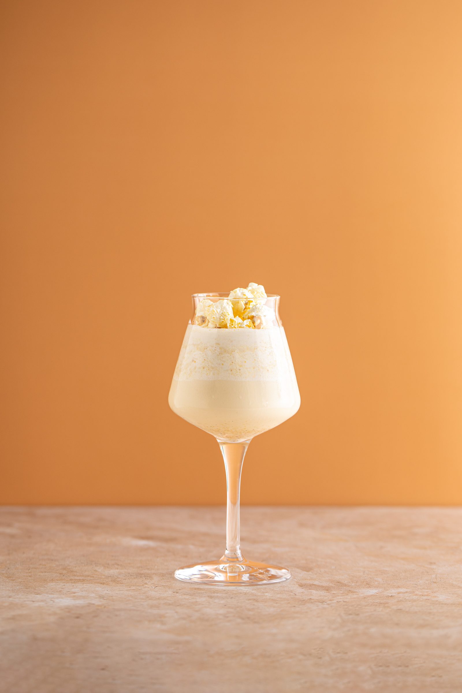 Heller Cocktail mit Popcorn im Stielglas vor orangefarbenem Hintergrund, Cocktailfoto für das Ludwig in Mosbach