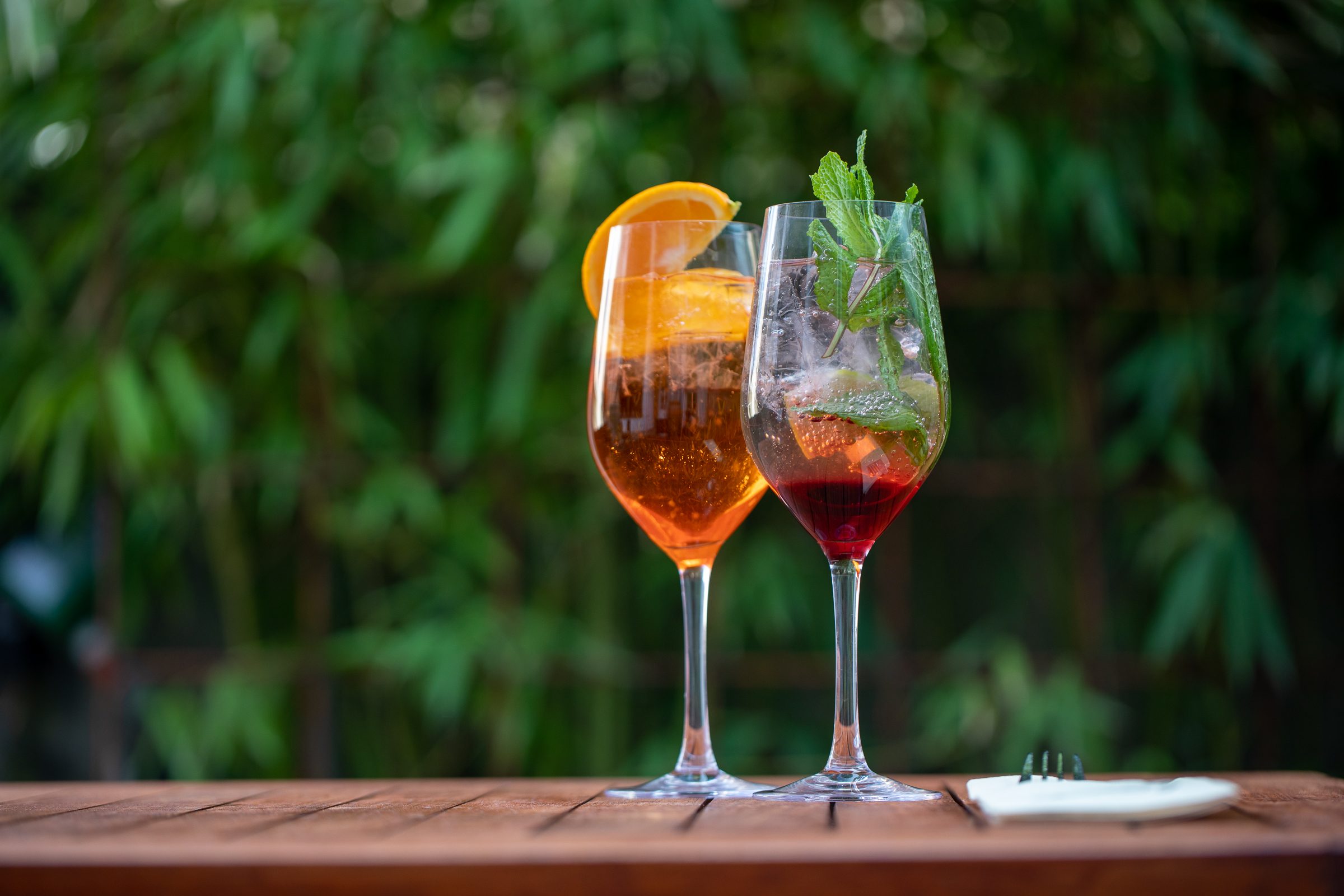 Zwei Spritz-Getränke mit Orange und Minze auf einem Holztisch im Freien vor grünem Bambus beim Ludwig in Mosbach