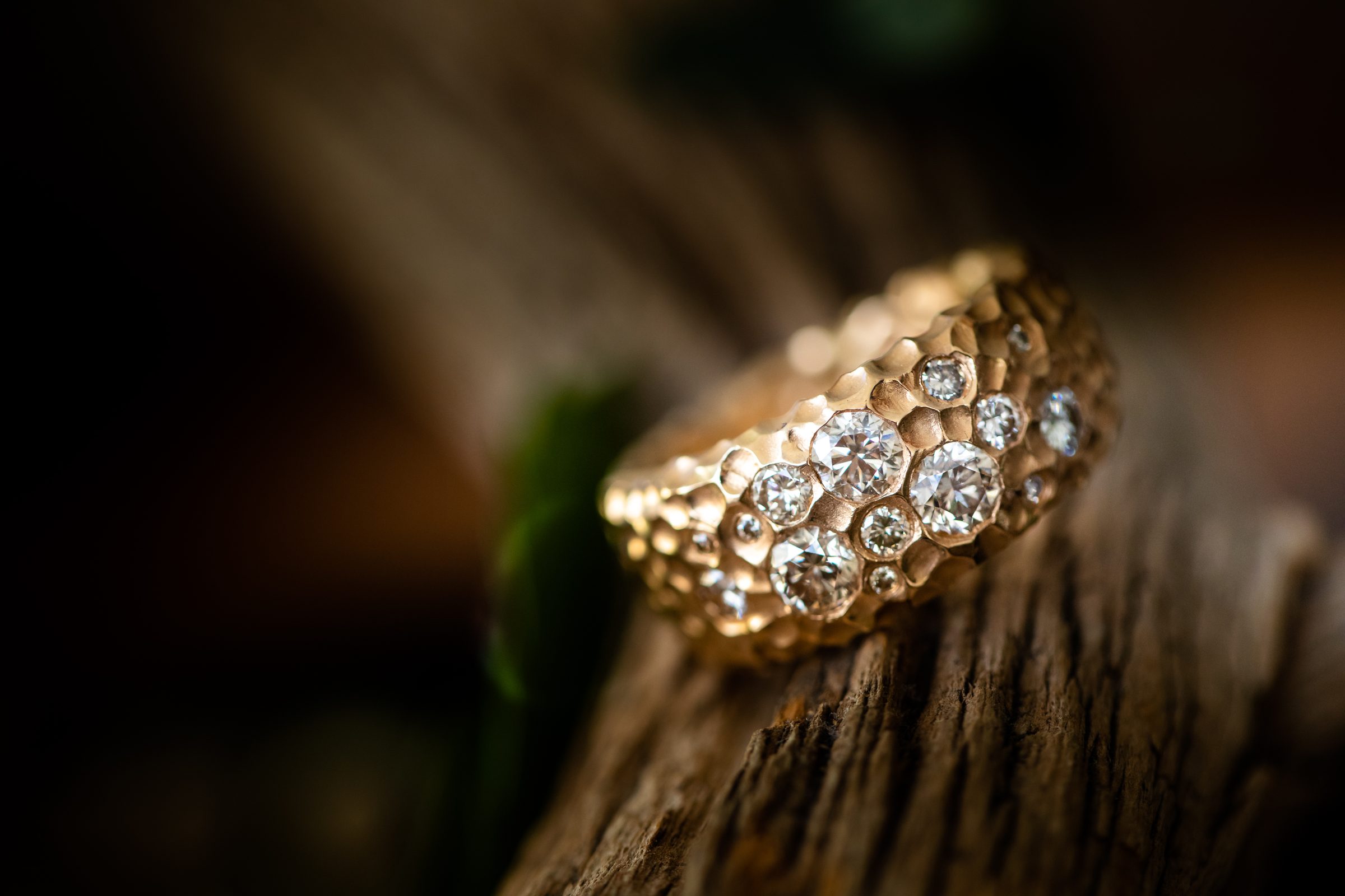 Goldener Ring mit vielen Diamanten auf einem Stück Holz vor dunklem Hintergrund