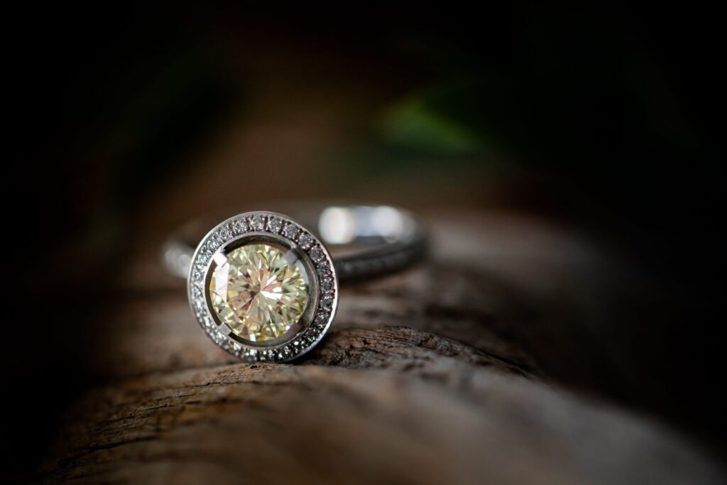 Ring mit großem hellgelbem Diamanten in einem Kranz aus kleinen Diamanten auf einem Stück Holz vor dunklem Hintergrund, Schmuck von Marion Knorr