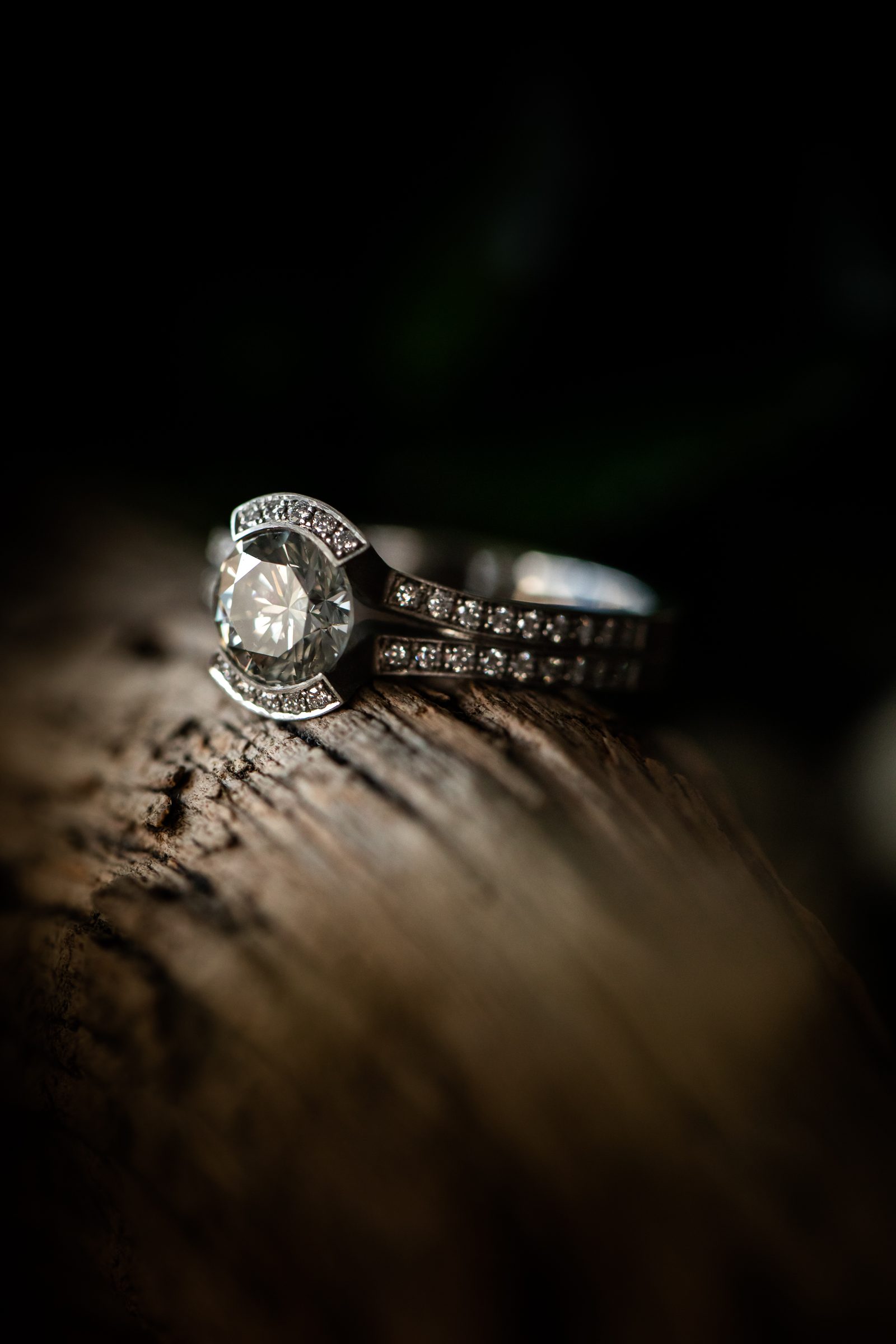 Silberfarbener Ring mit Diamant in breiter Fassung und kleinen Diamanten auf der Ringschiene auf einem Stück Holz, Schmuck von Marion Knorr
