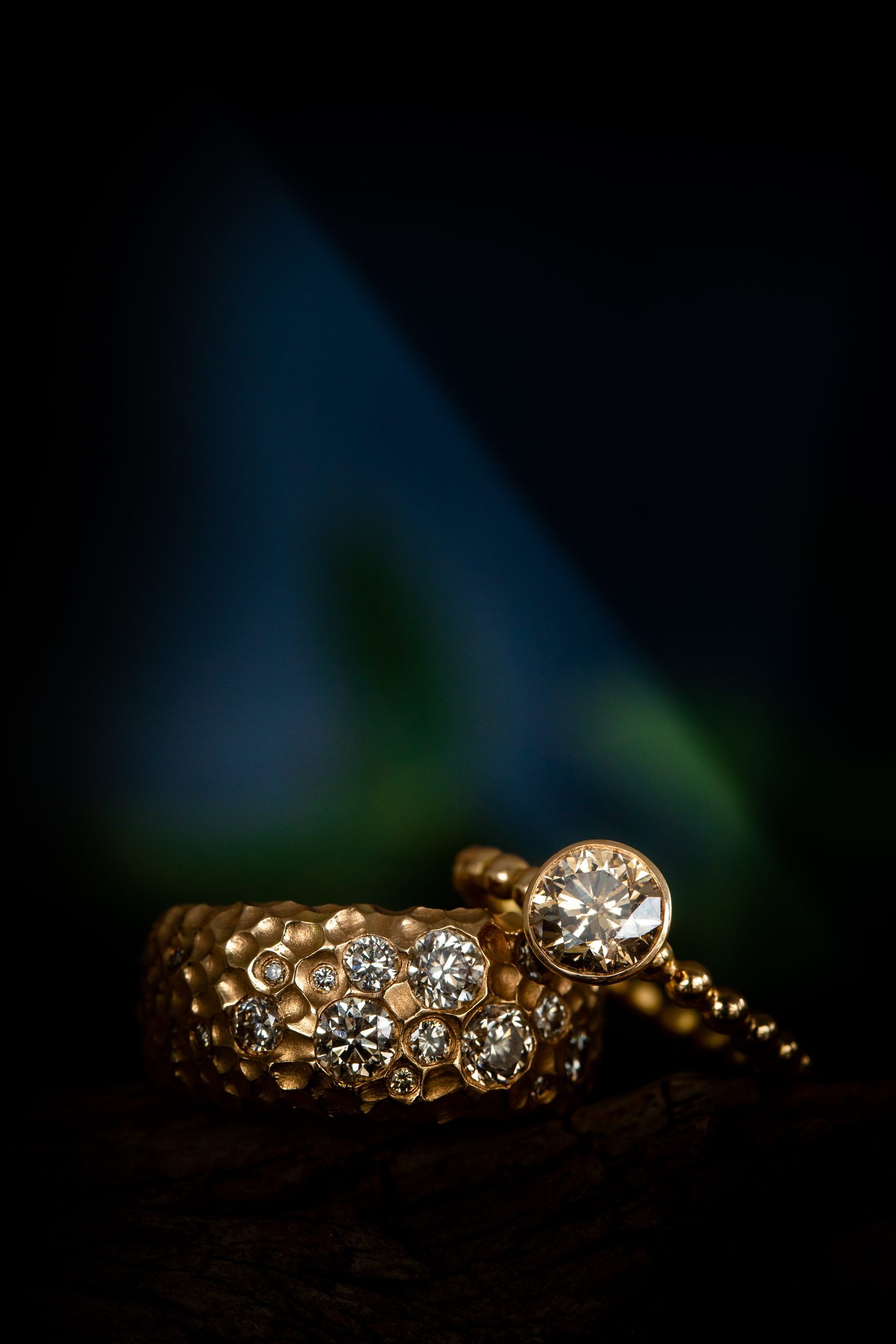 Breiter Goldring mit vielen eingelassenen Diamanten und ein schmaler Goldring mit Solitär vor dunklem Hintergrund, Schmuck von Marion Knorr