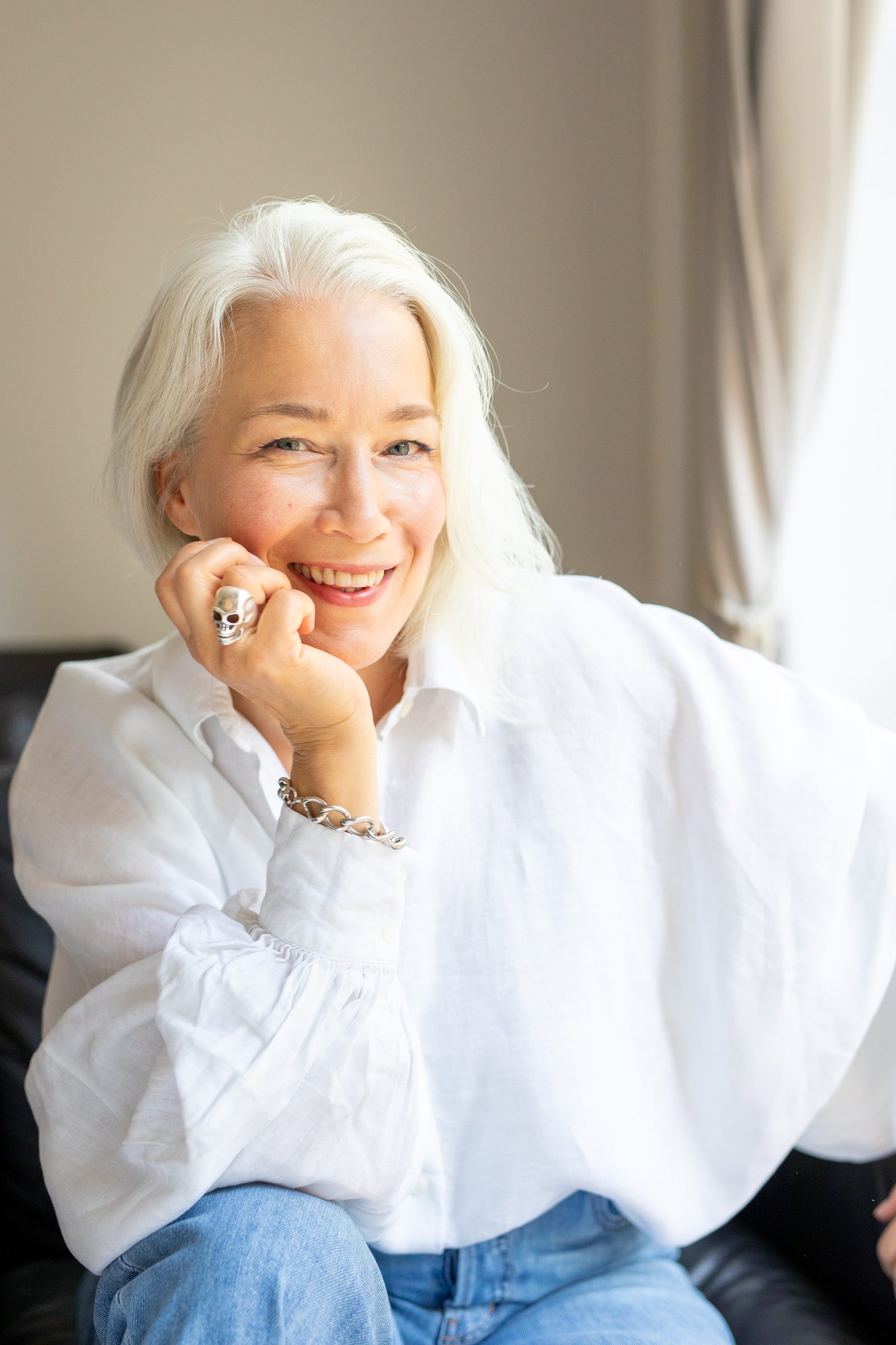 Porträt von Nina Goldhammer in weißer Bluse, lächelnd mit dem Kinn in der Hand in einem Ledersessel