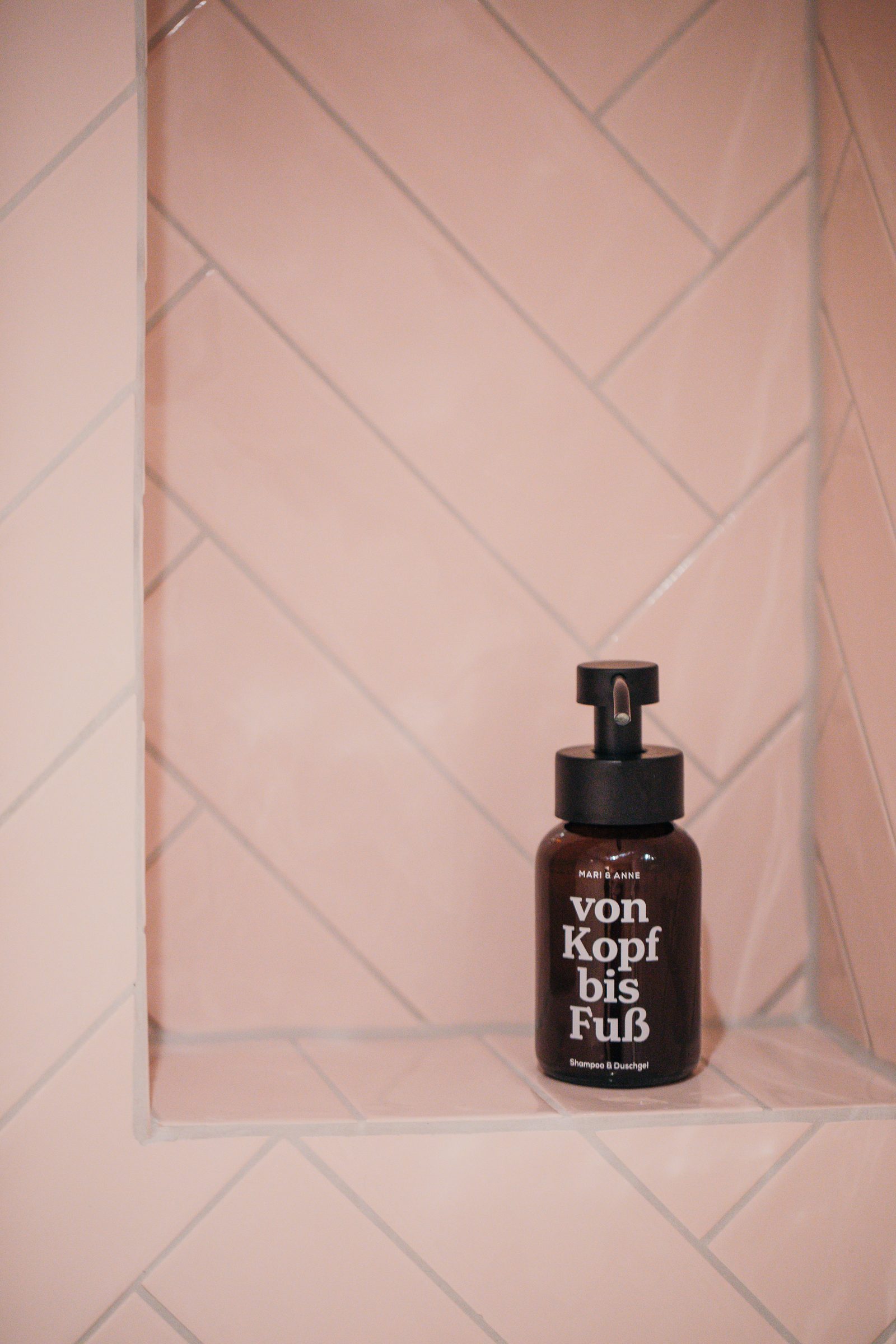 Flasche Seife mit der Aufschrift von Kopf bis Fuß in einer rosa gefliesten Wandnische