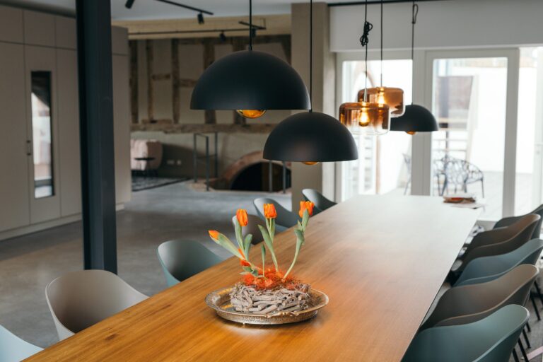 Lange Holztafel mit grauen Stühlen und Tulpengesteck unter schwarzen und kupferfarbenen Pendelleuchten im Ois is gut, dahinter altes Fachwerk