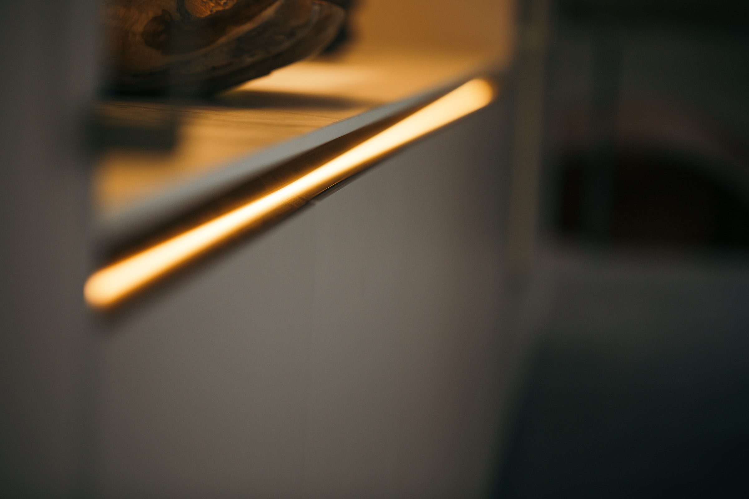 Warm leuchtendes Lichtband unter einem Regalboden an einer hellen Schrankfront
