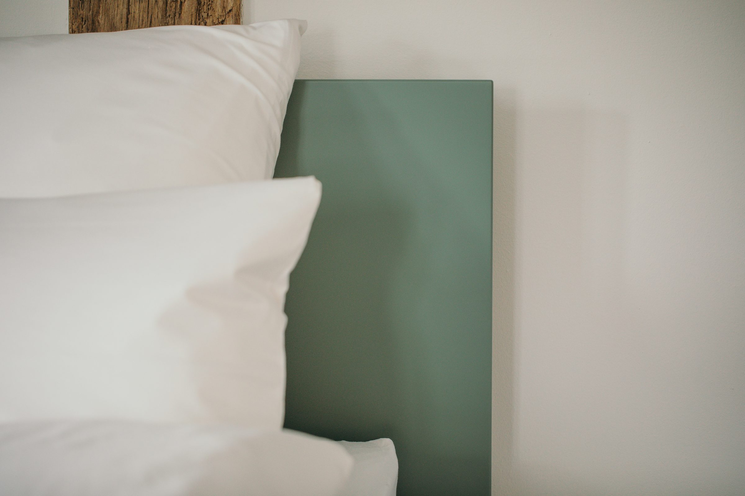 Weiße Kopfkissen vor einem salbeigrünen Kopfteil an einer hellen Wand