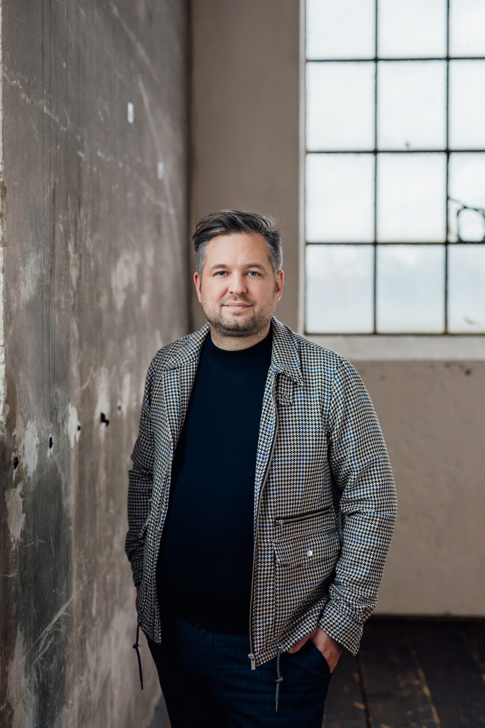 Porträt von Johannes Hüsch in karierter Jacke vor einer Betonwand