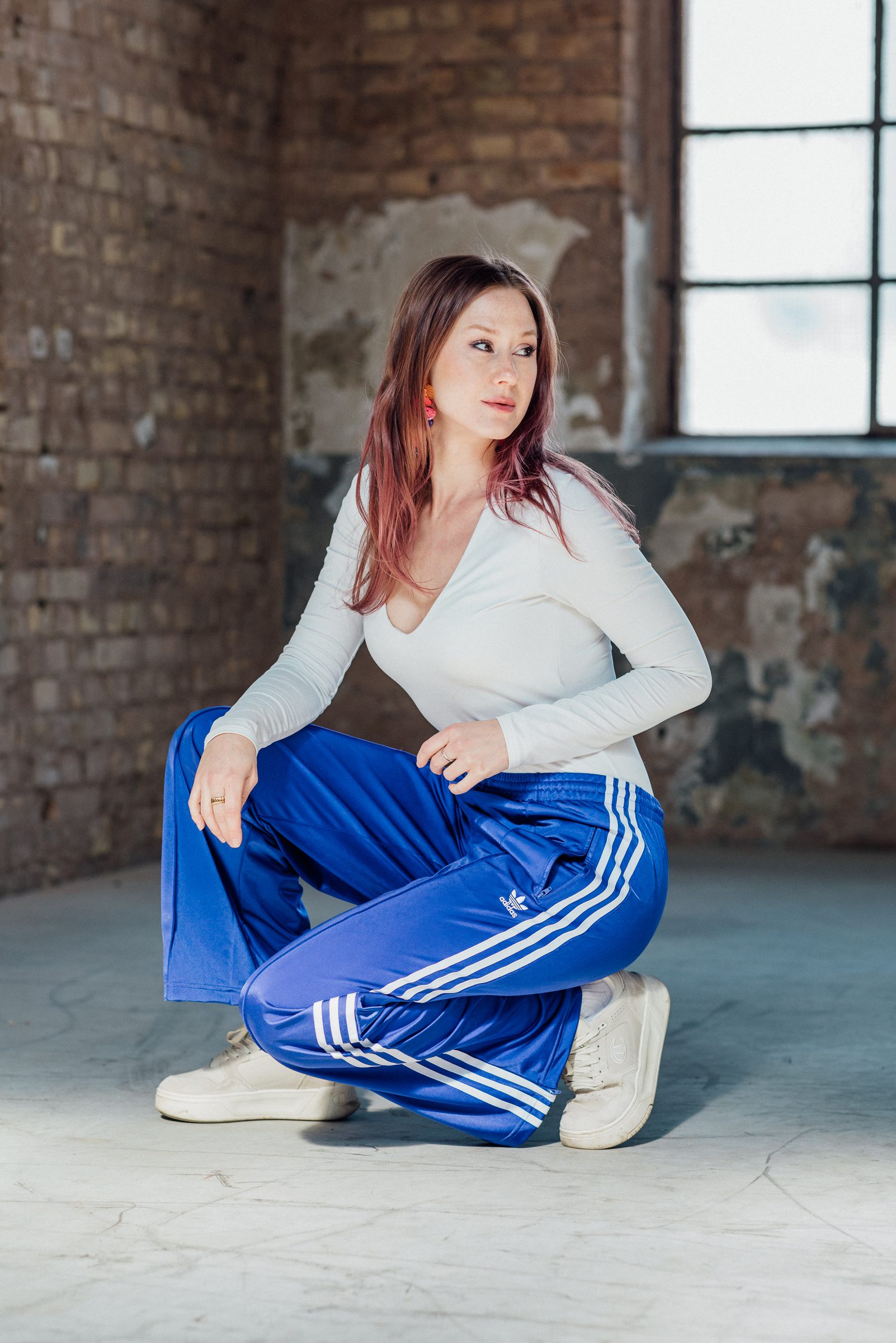 Sasha Walker hockt in blauer Trainingshose in der Industriehalle und blickt zur Seite