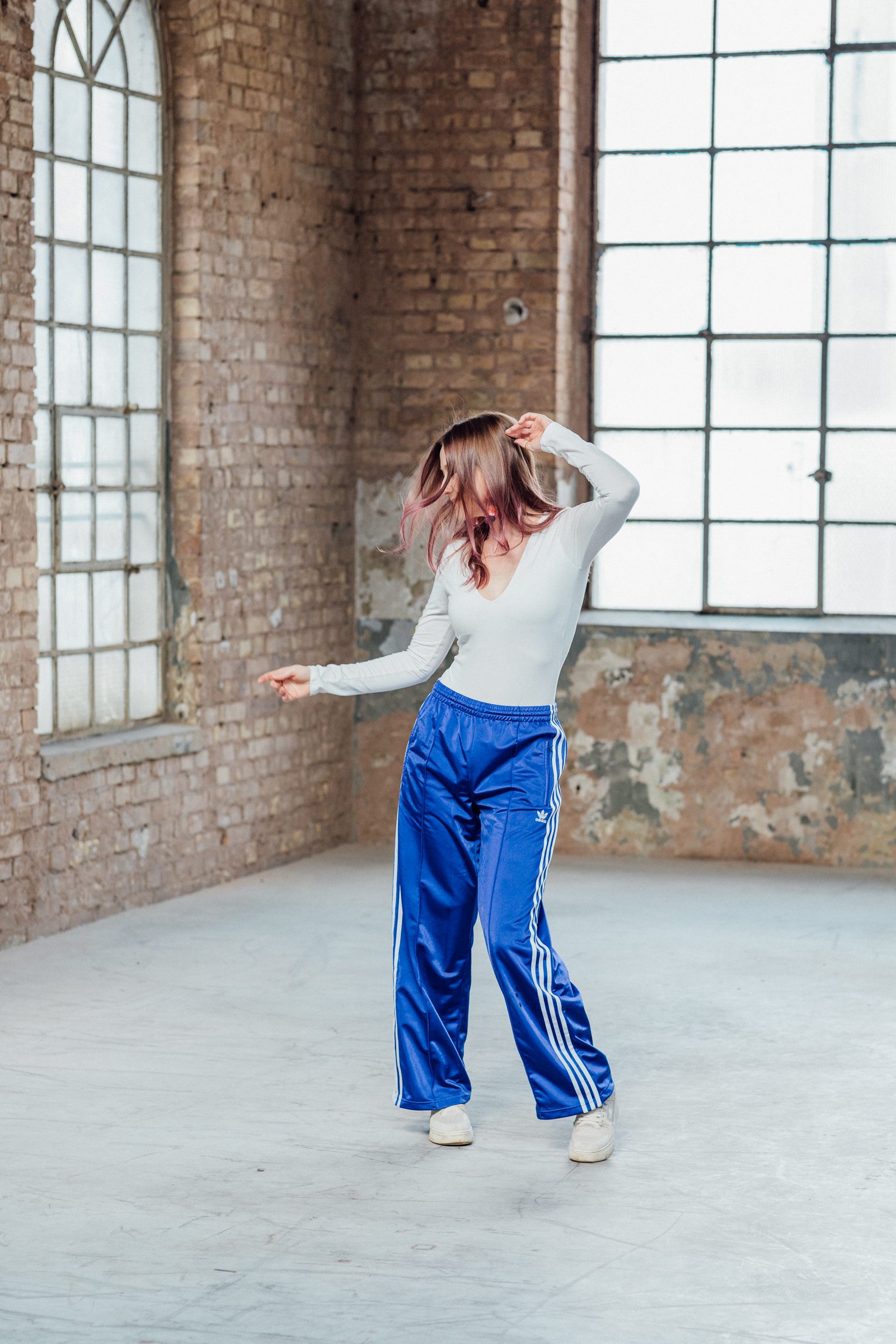 Sasha Walker tanzt in blauer Trainingshose durch eine helle Industriehalle mit hohen Fenstern