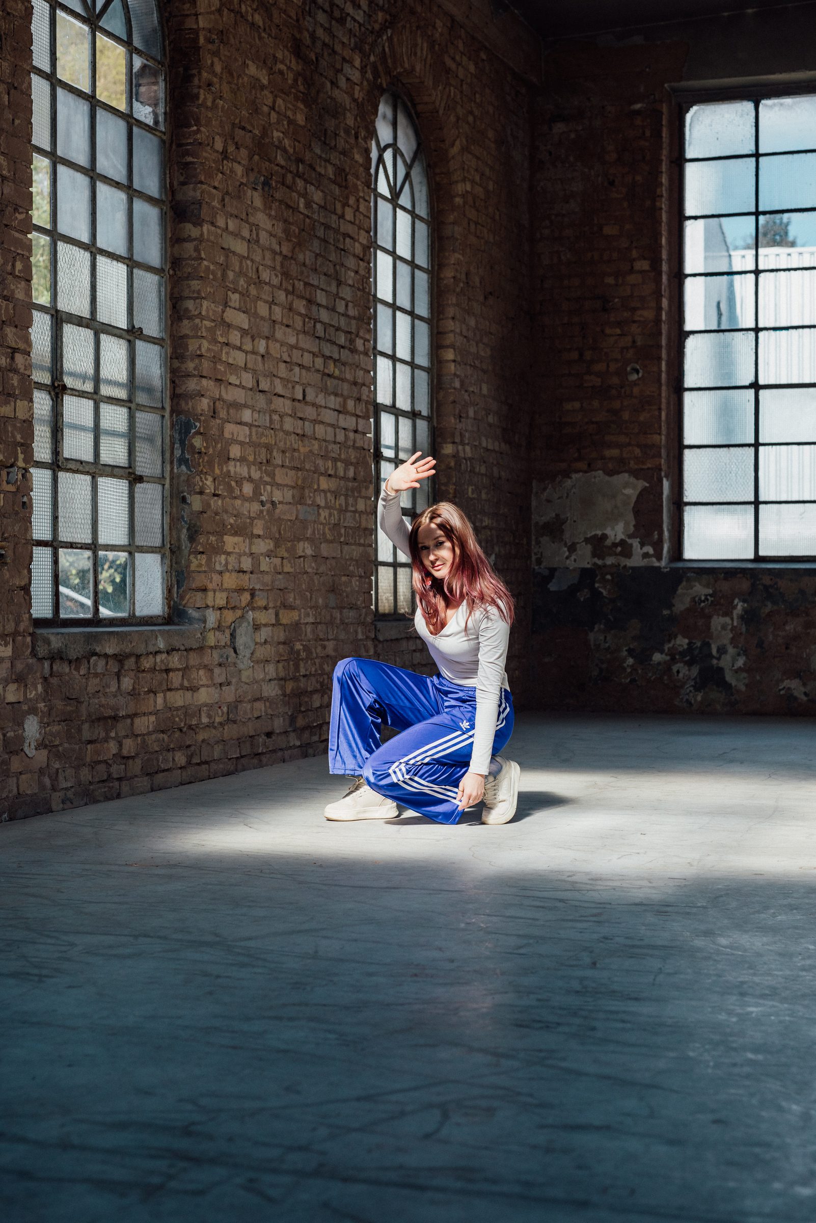 Sasha Walker kniet in einem Lichtstreifen in einer dunklen Industriehalle mit hohen Fenstern