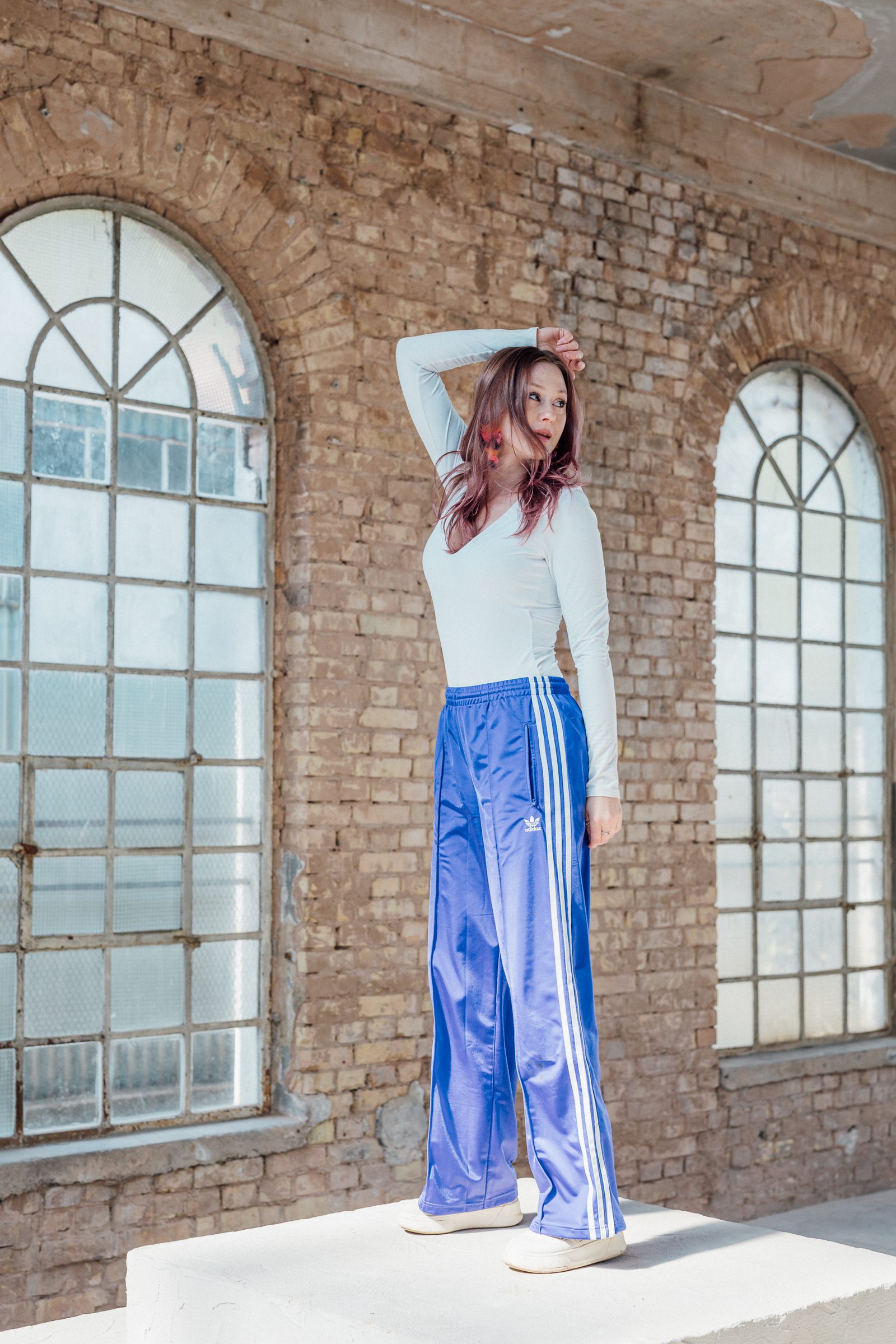 Sasha Walker steht mit einer Hand am Kopf auf einem Betonpodest zwischen zwei Rundbogenfenstern