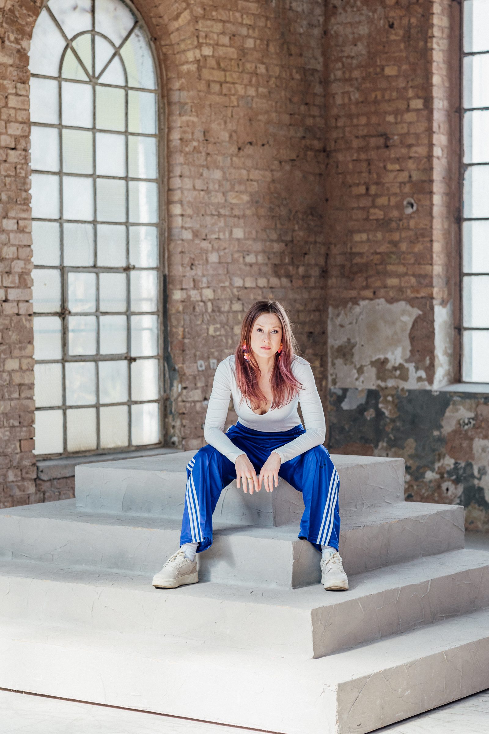 Sasha Walker sitzt auf einer Betontreppe in der Mitte einer Industriehalle mit Rundbogenfenstern
