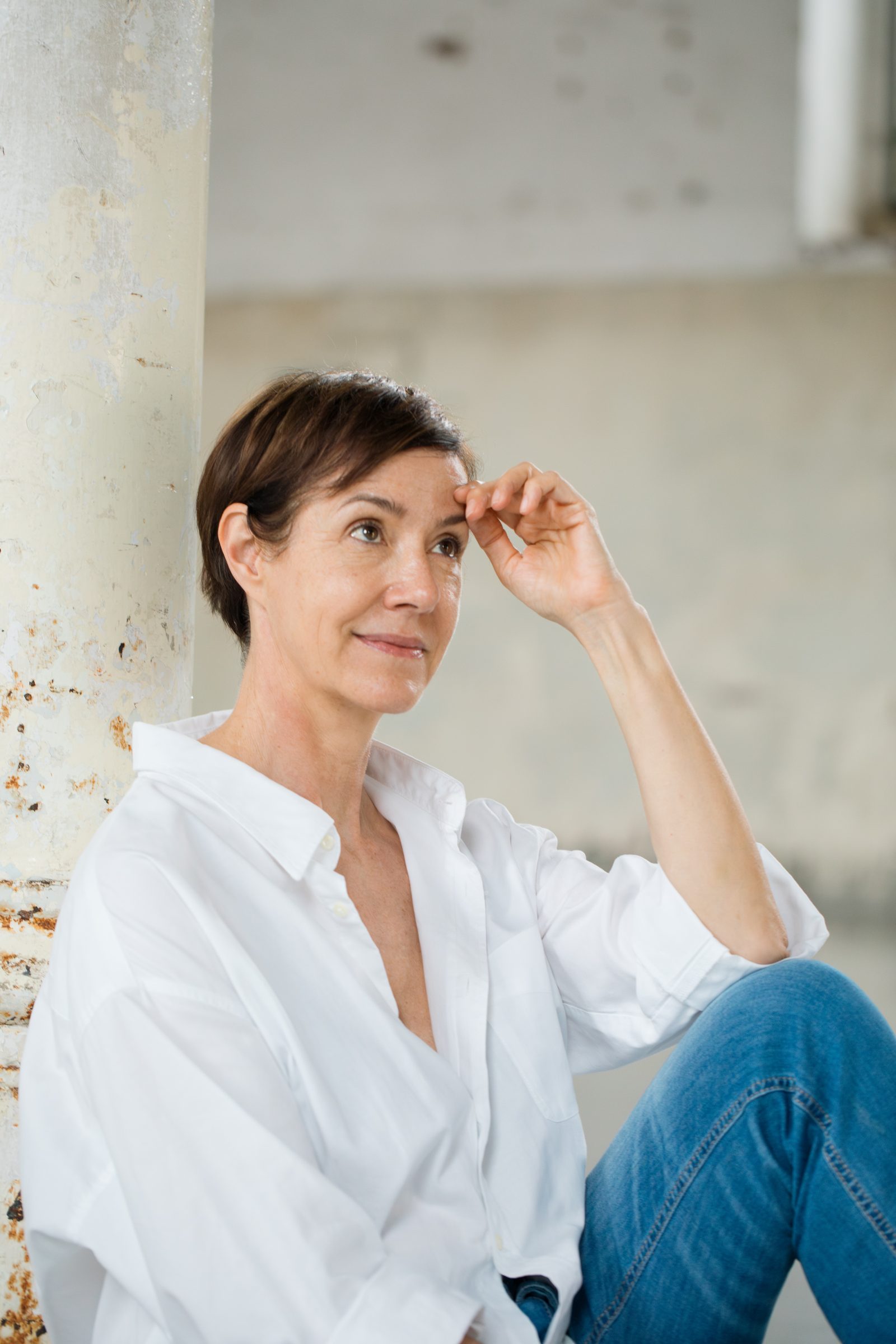 Frau in weißer Bluse und Jeans sitzt entspannt und streicht sich durchs Haar, Personal-Branding-Porträt für Schminktante
