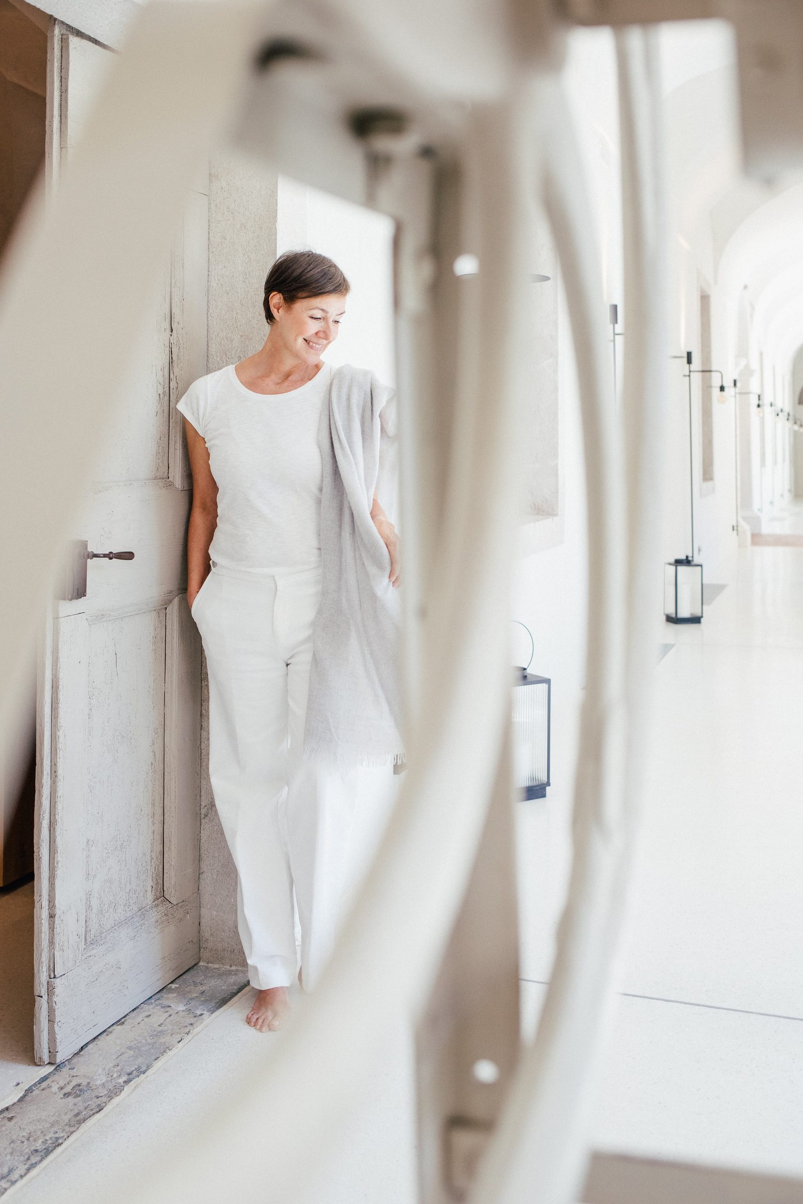 Frau in Weiß lehnt an einer alten Tür, durch einen hellen Rahmen im Vordergrund fotografiert, Personal-Branding-Porträt für Schminktante