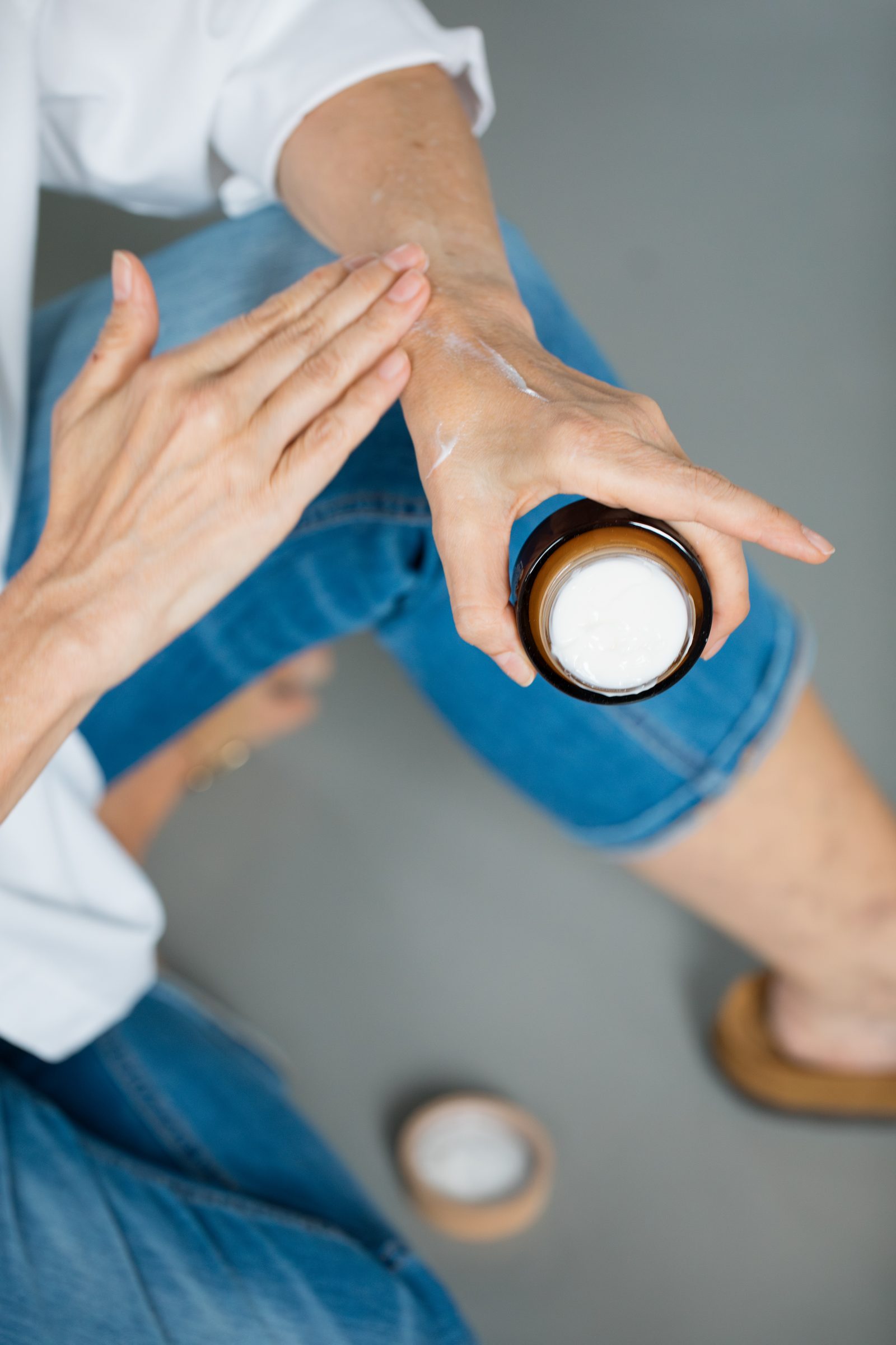 Hände verteilen Creme aus einem kleinen Tiegel auf dem Handrücken