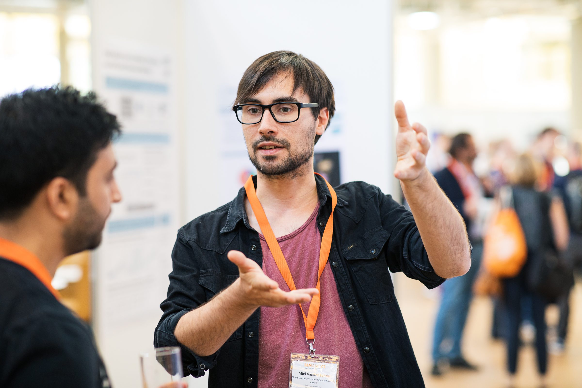 Teilnehmer der Konferenz SEMANTiCS erklärt im Gespräch mit erhobener Hand etwas, im Hintergrund weitere Gäste