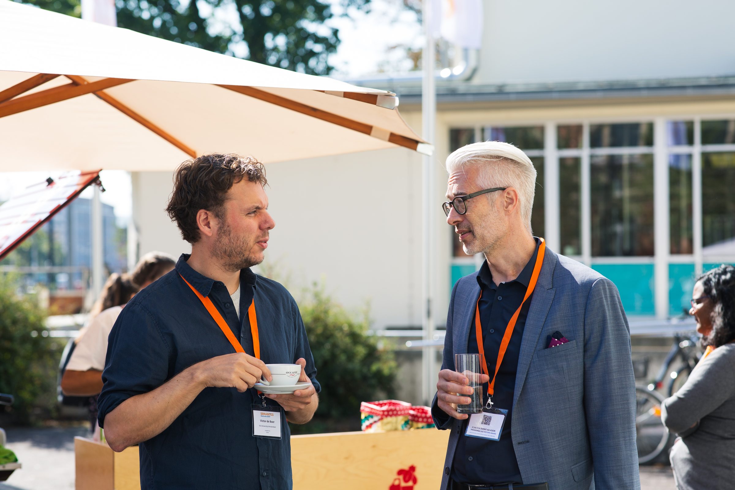 Zwei Teilnehmer der Konferenz SEMANTiCS unterhalten sich in der Pause unter einem Sonnenschirm, einer mit Kaffeetasse