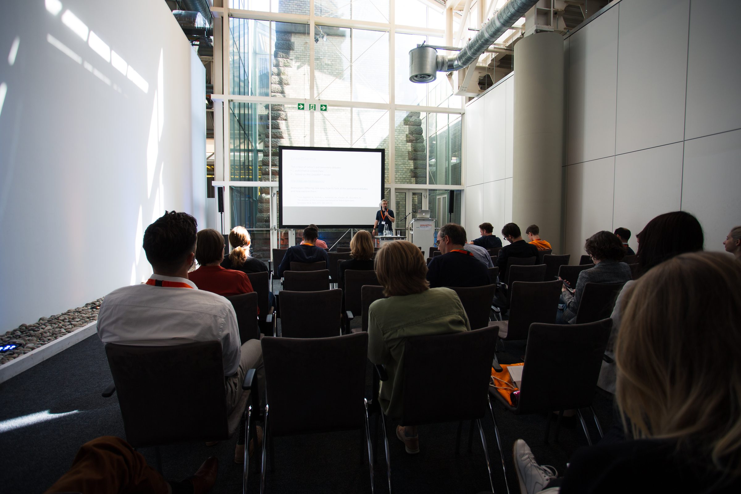 Publikum in einem kleineren Vortragsraum der Konferenz SEMANTiCS, vorne ein Redner vor der Leinwand