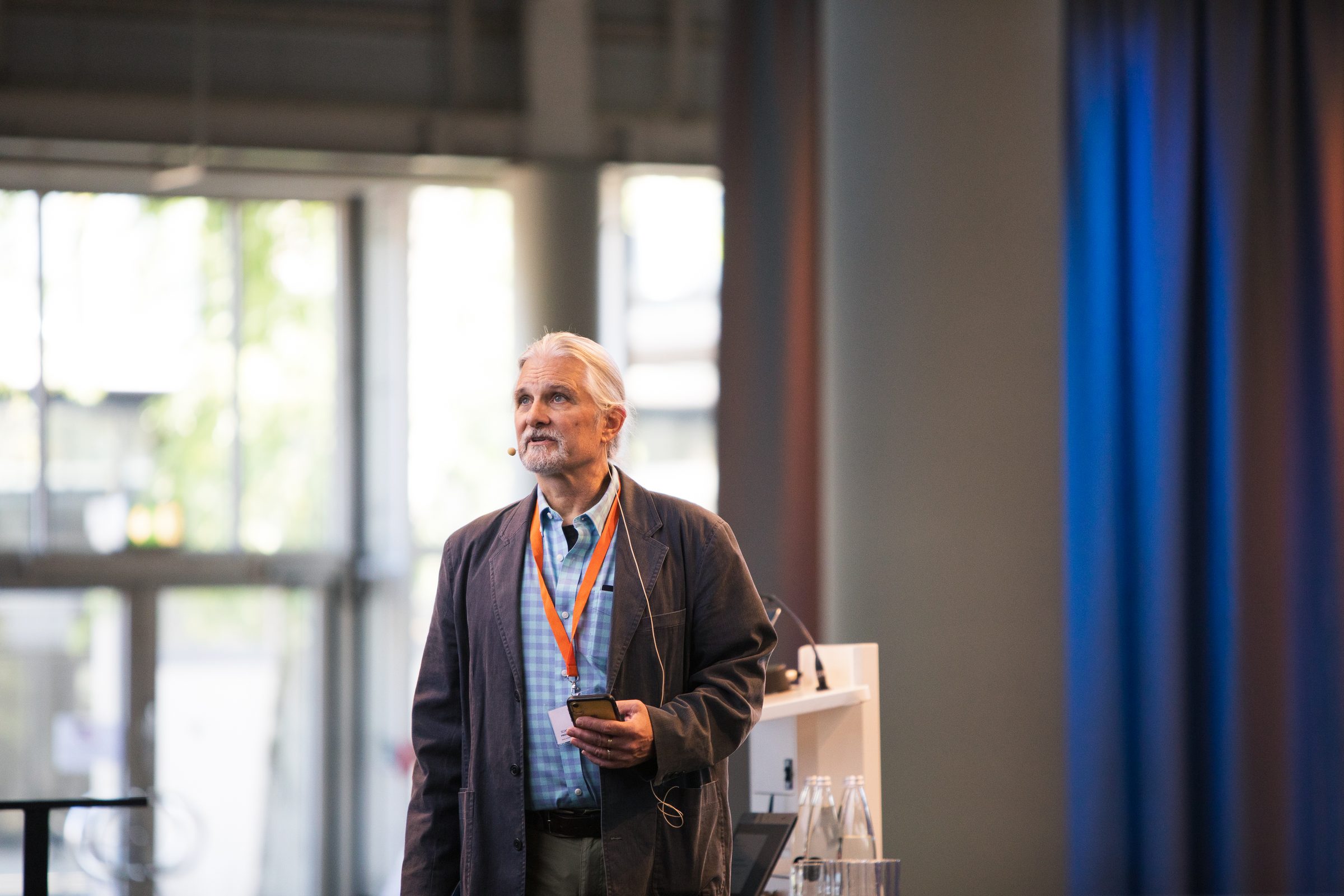 Redner mit Headset-Mikrofon und Smartphone in der Hand steht neben dem Rednerpult der Konferenz SEMANTiCS