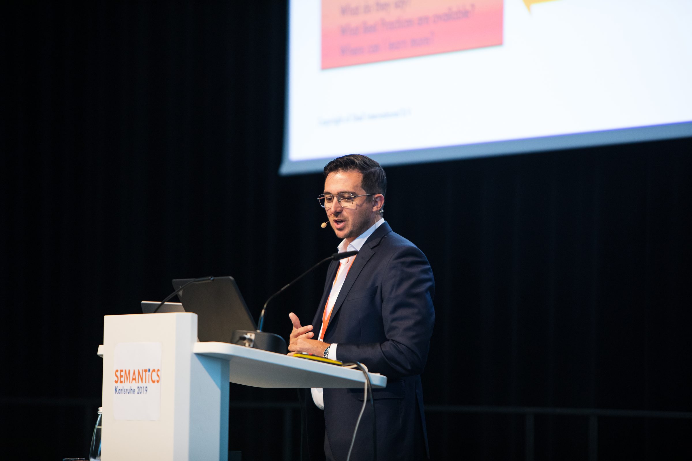 Redner am Rednerpult mit dem Logo der Konferenz SEMANTiCS, dahinter seine Präsentation auf der Leinwand