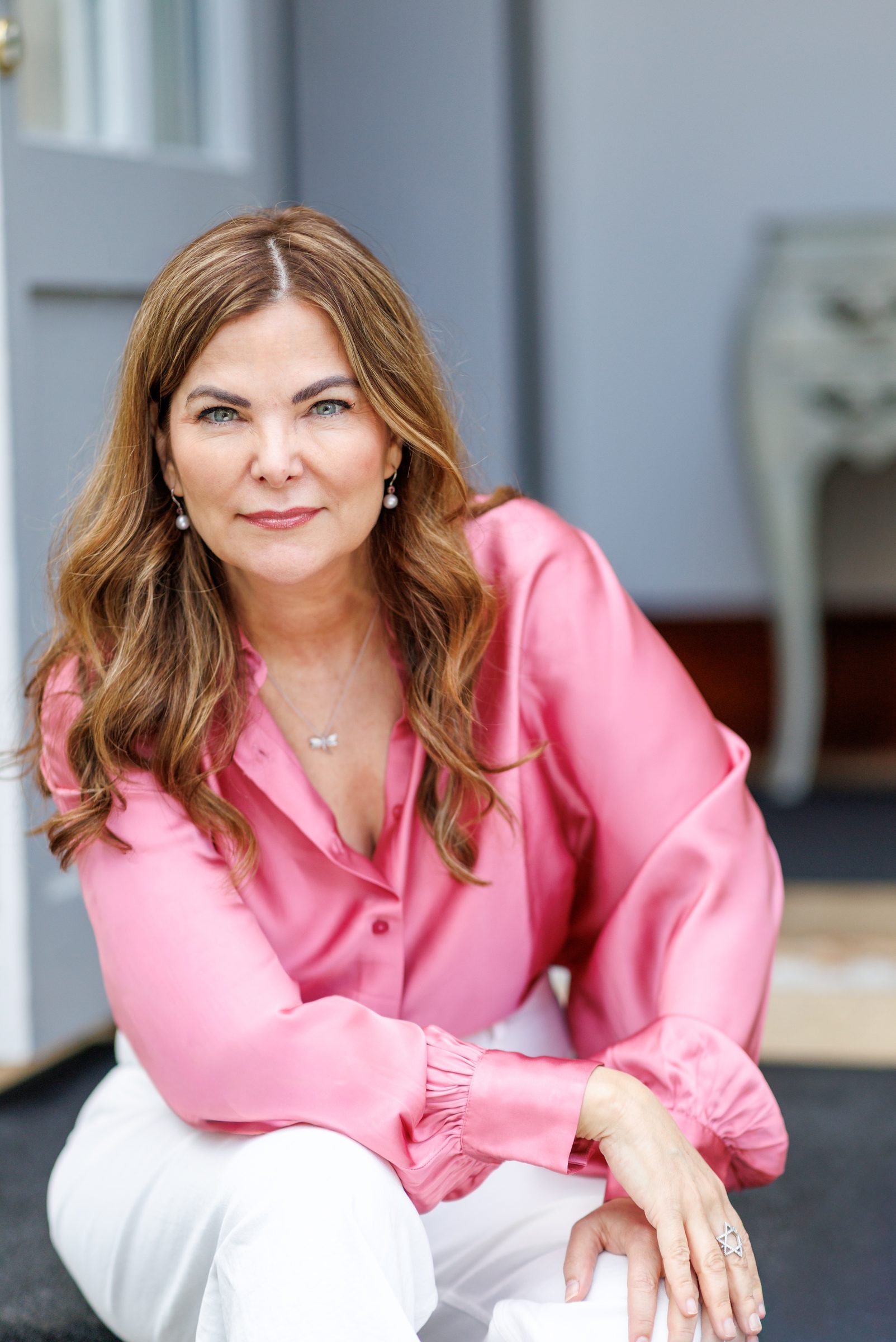 Porträt von Sheila de Liz in pinker Satinbluse, sitzend in einem hellen Raum