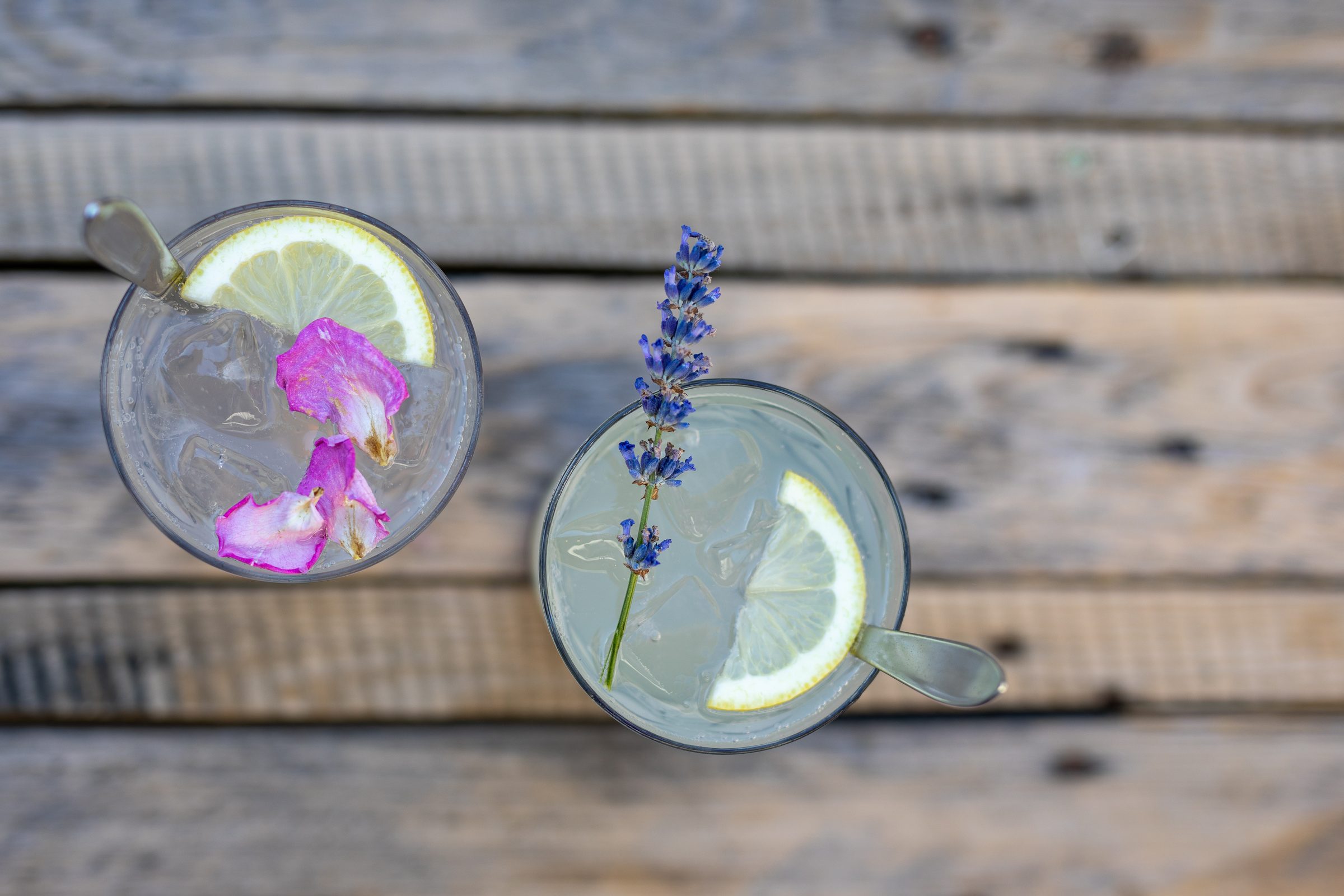 Zwei Gläser Limonade mit Zitronenscheiben, Blüten und Lavendel auf einem Holztisch, von oben fotografiert