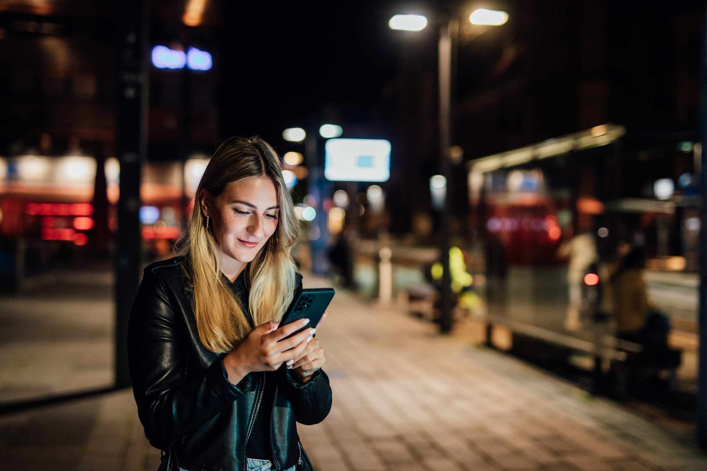 Junge Frau schaut nachts an einer Haltestelle auf ihr Smartphone, Kampagne der Stadtwerke Heilbronn
